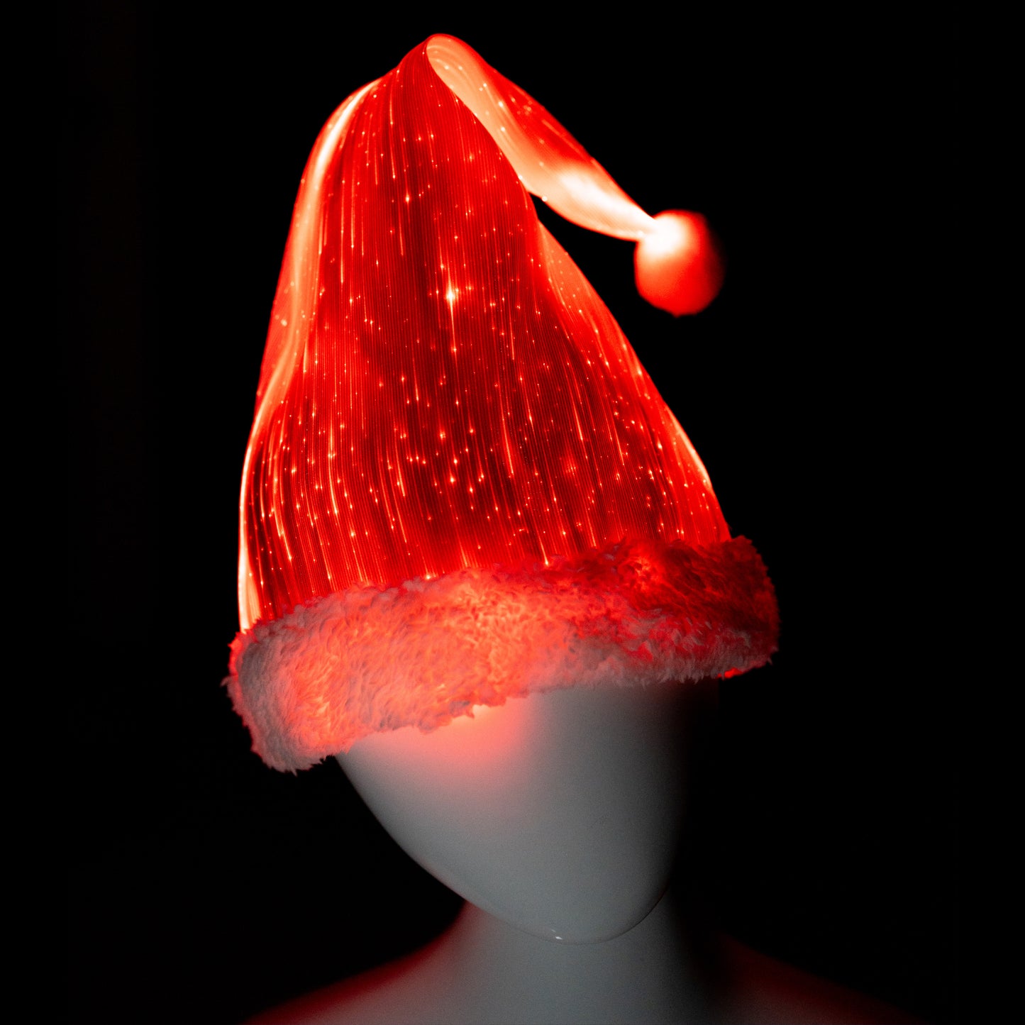 Fiber optic light-up Santa hat glowing in red light on a mannequin head against a dark background