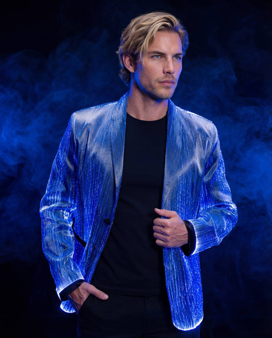 Man wearing a glowing blue fiber-optic suit jacket, standing against a dark blue smoke-filled background with one hand in his pocket