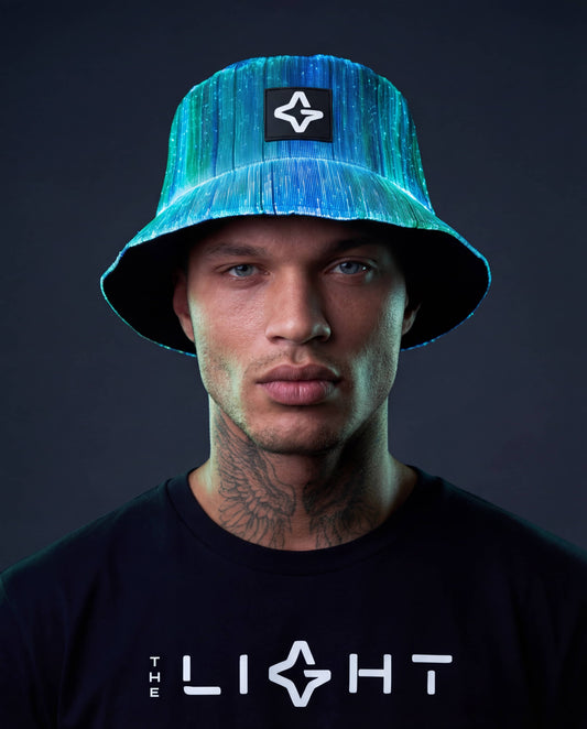Person wearing a blue fiber optic light-up bucket hat and a black “THE LIGHT” t-shirt against a dark background