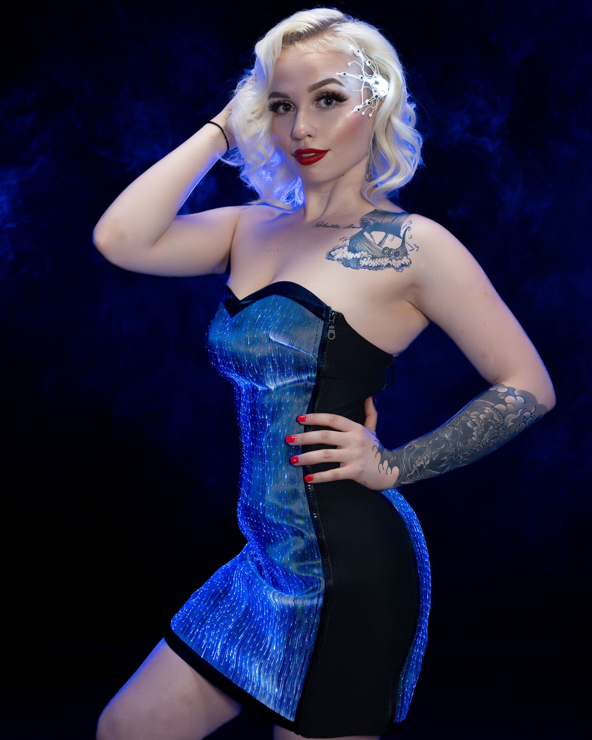 Woman wearing a strapless fiber optic light-up dress illuminated in blue light against a dark background