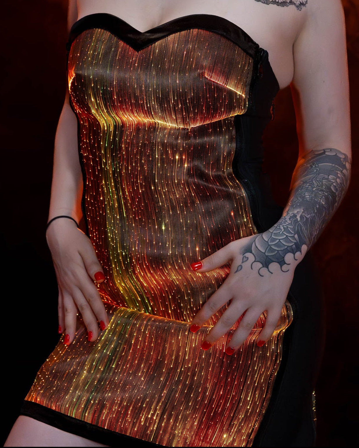 Woman wearing a strapless fiber optic light-up dress illuminated in orange light against a dark background