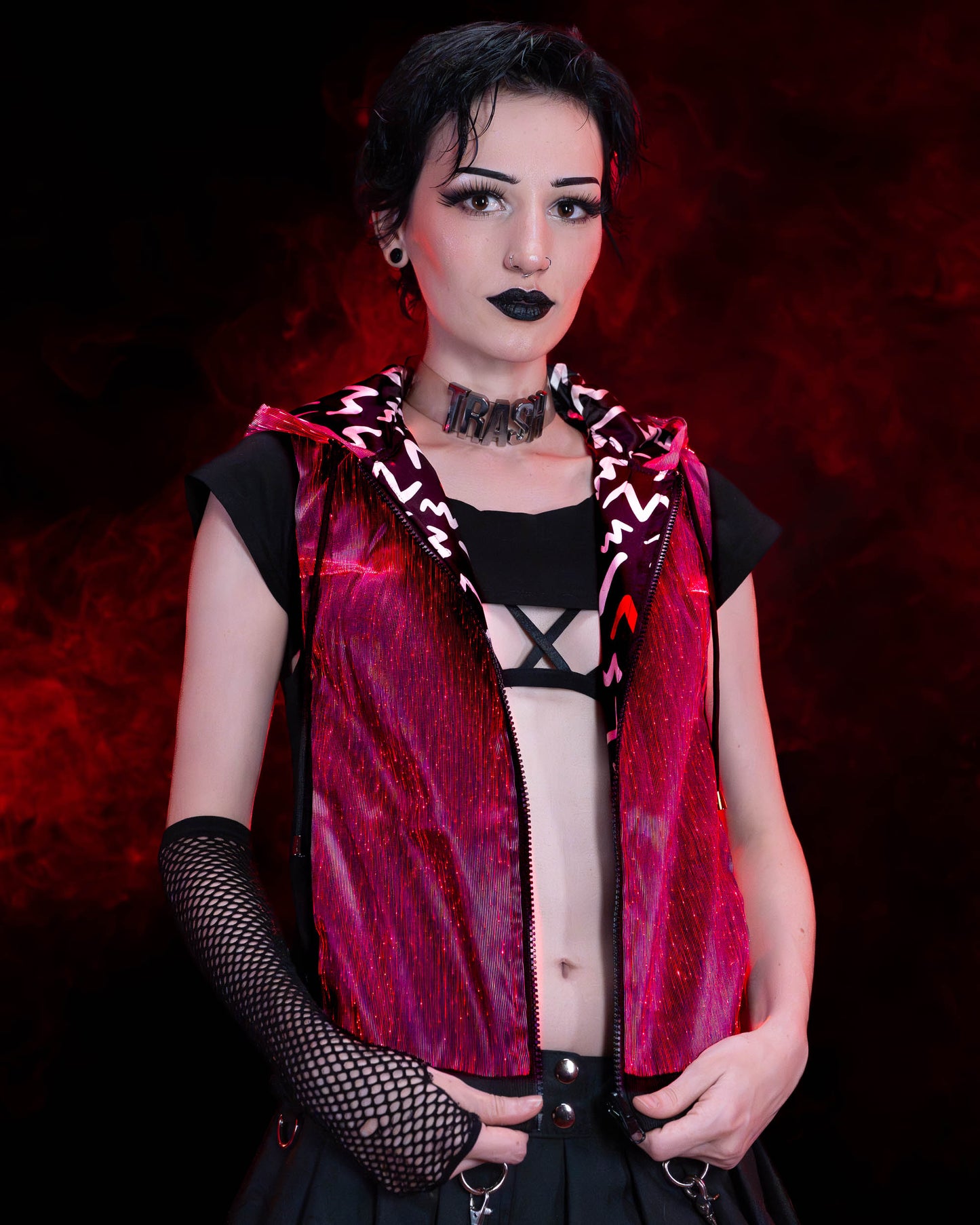 Woman wearing a black fiber optic light up sleeveless hoodie glowing in red light against a dark background