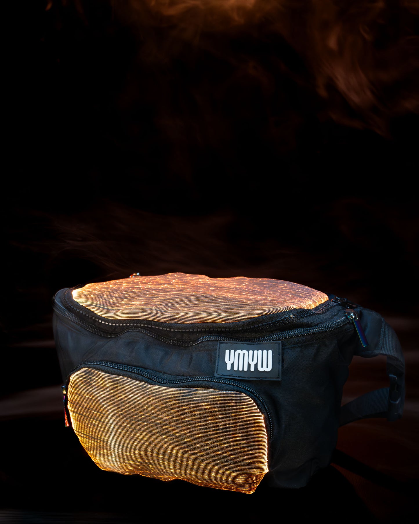 Fiber optic light up waist bag illuminated in orange light with "YMYW" branding on a dark background