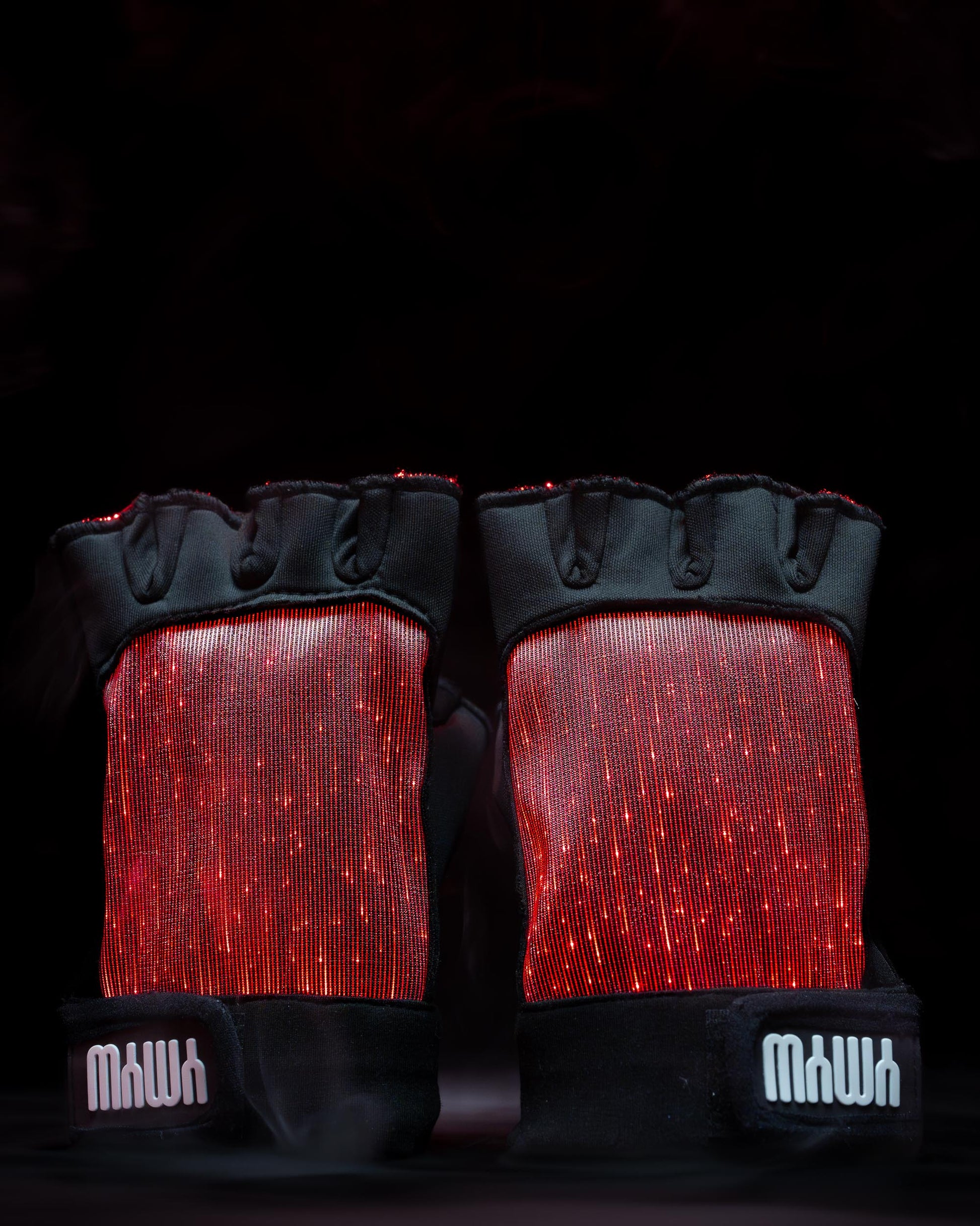 Pair of black fiber optic light up gloves illuminated in red light against a dark background