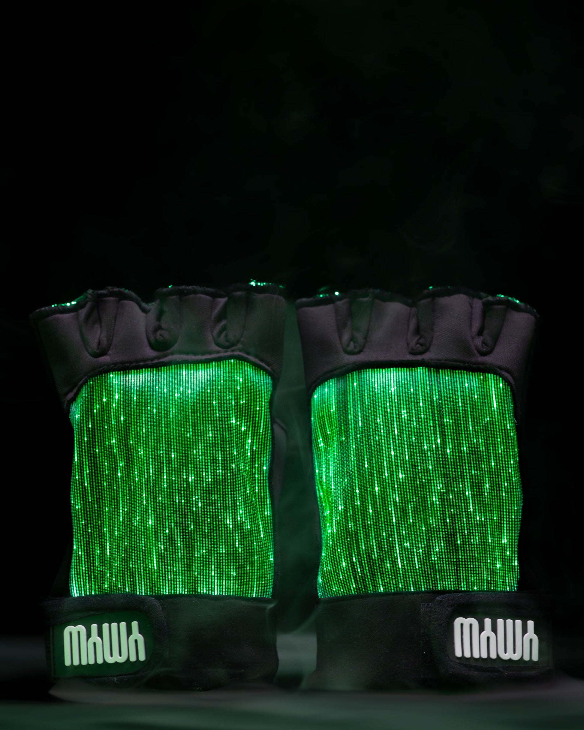 Pair of black fiber optic light up gloves illuminated in green light against a dark background