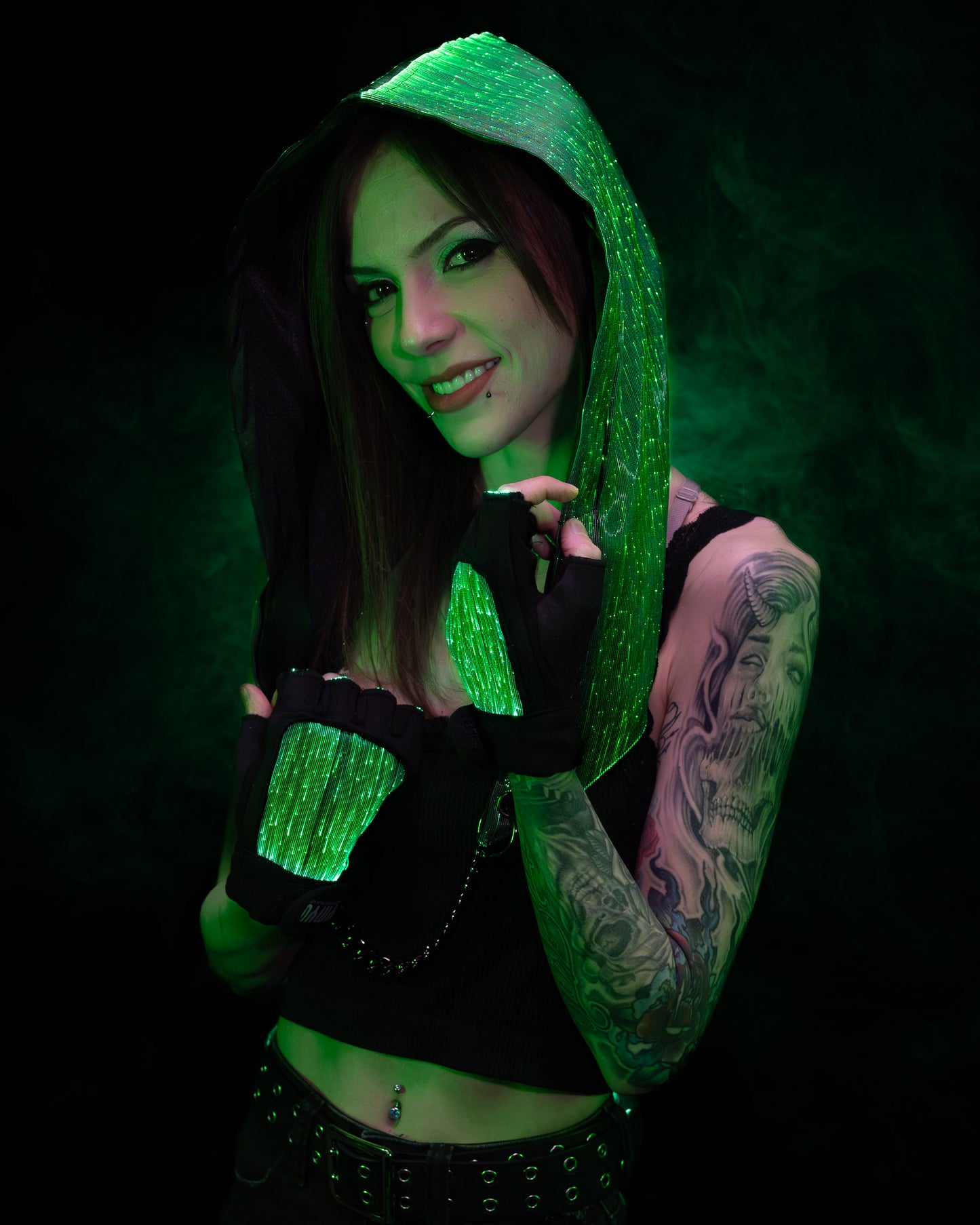 Woman wearing a fiber optic light-up hood and gloves illuminated in green light against a dark background