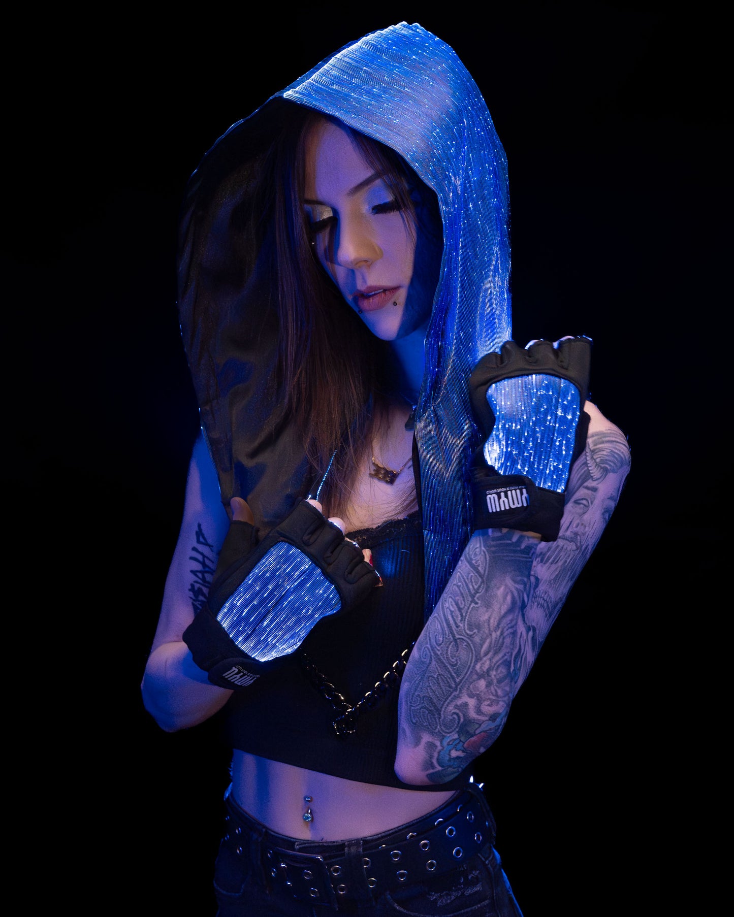 Woman wearing a fiber optic light-up hood and gloves illuminated in blue light against a dark background