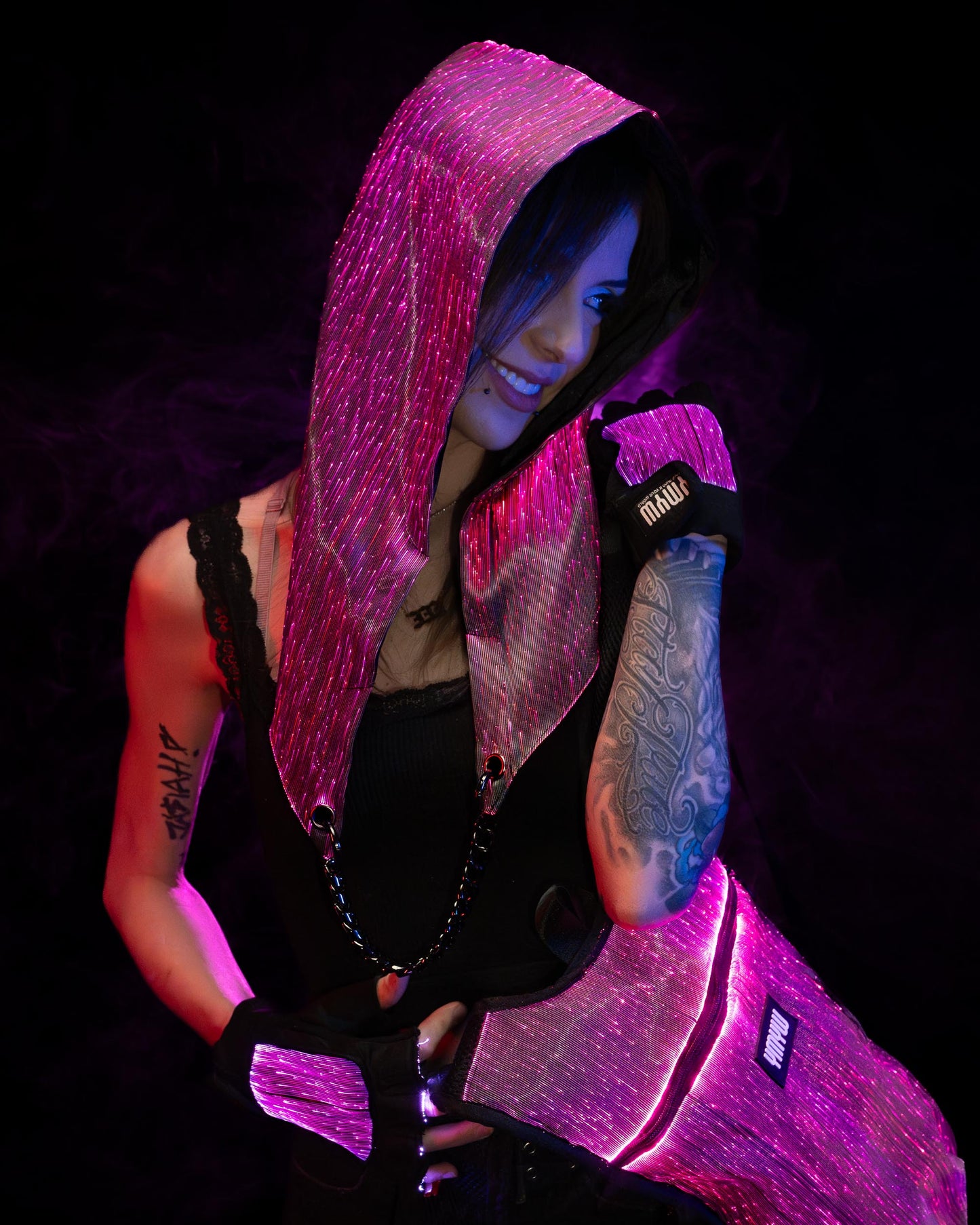 Woman wearing a fiber optic light-up hood and gloves illuminated in pink light against a dark background