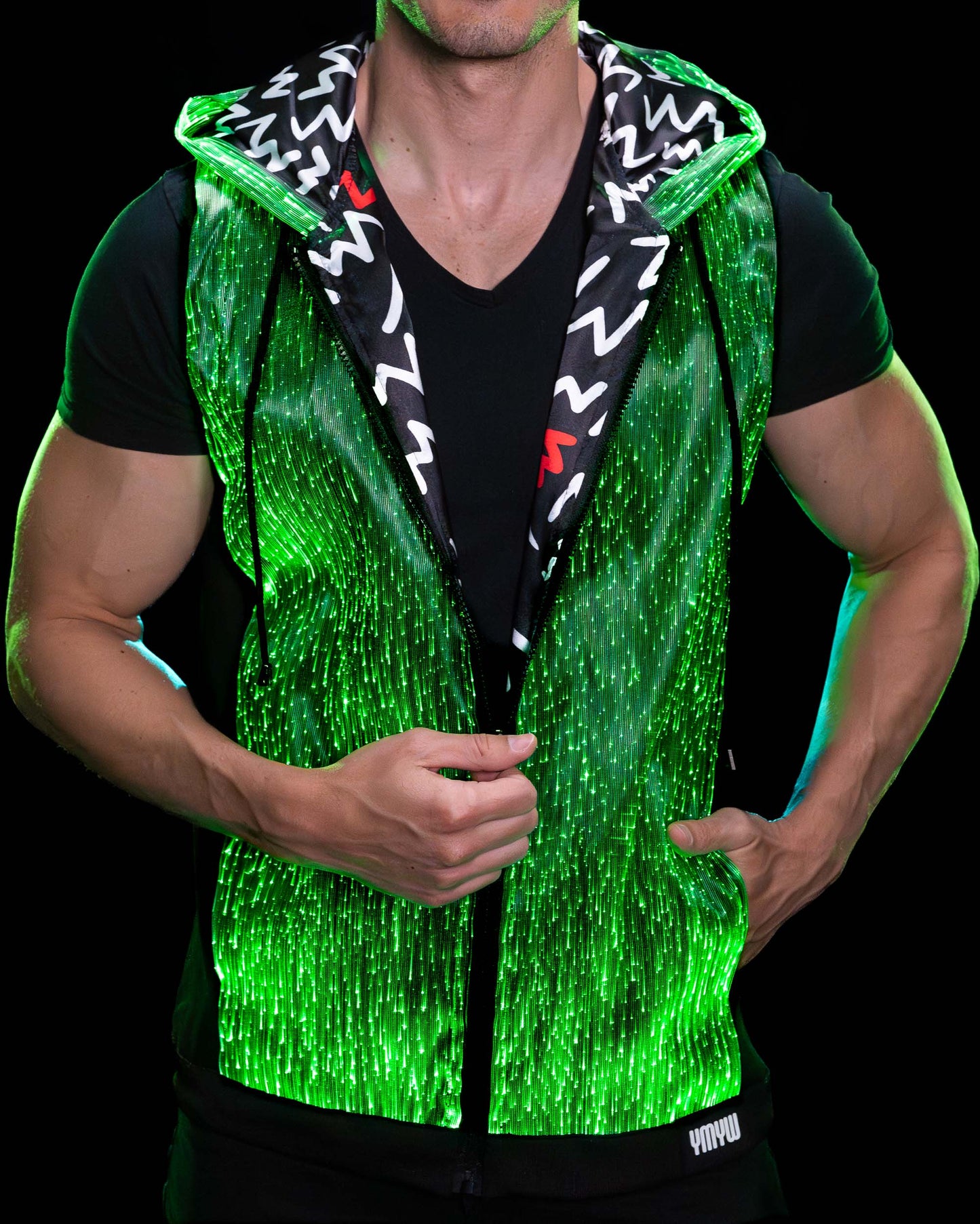 Man wearing a fiber optic light-up sleeveless hoodie illuminated in green against a dark background