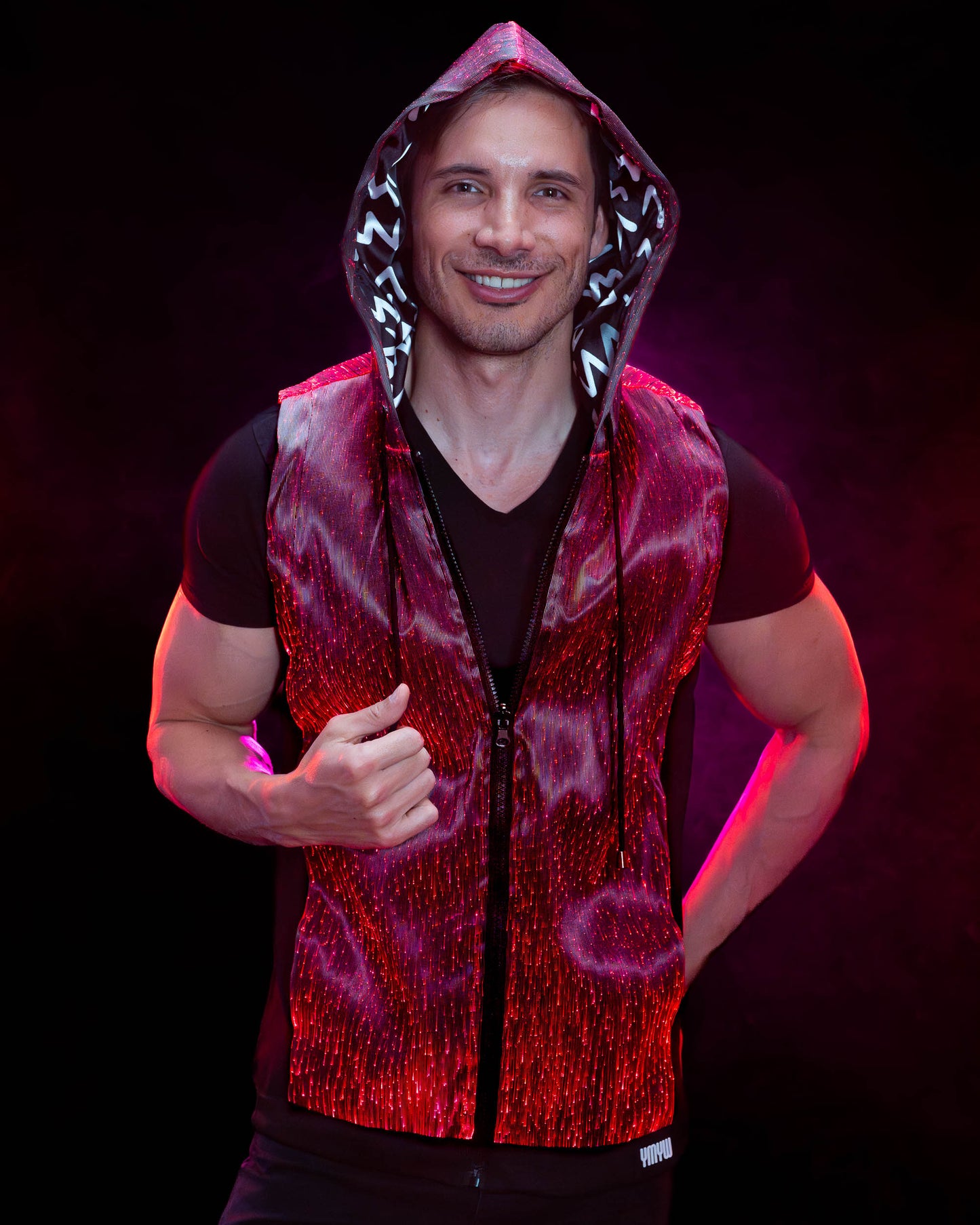 Man wearing a fiber optic light-up sleeveless hoodie illuminated in red light against a dark background
