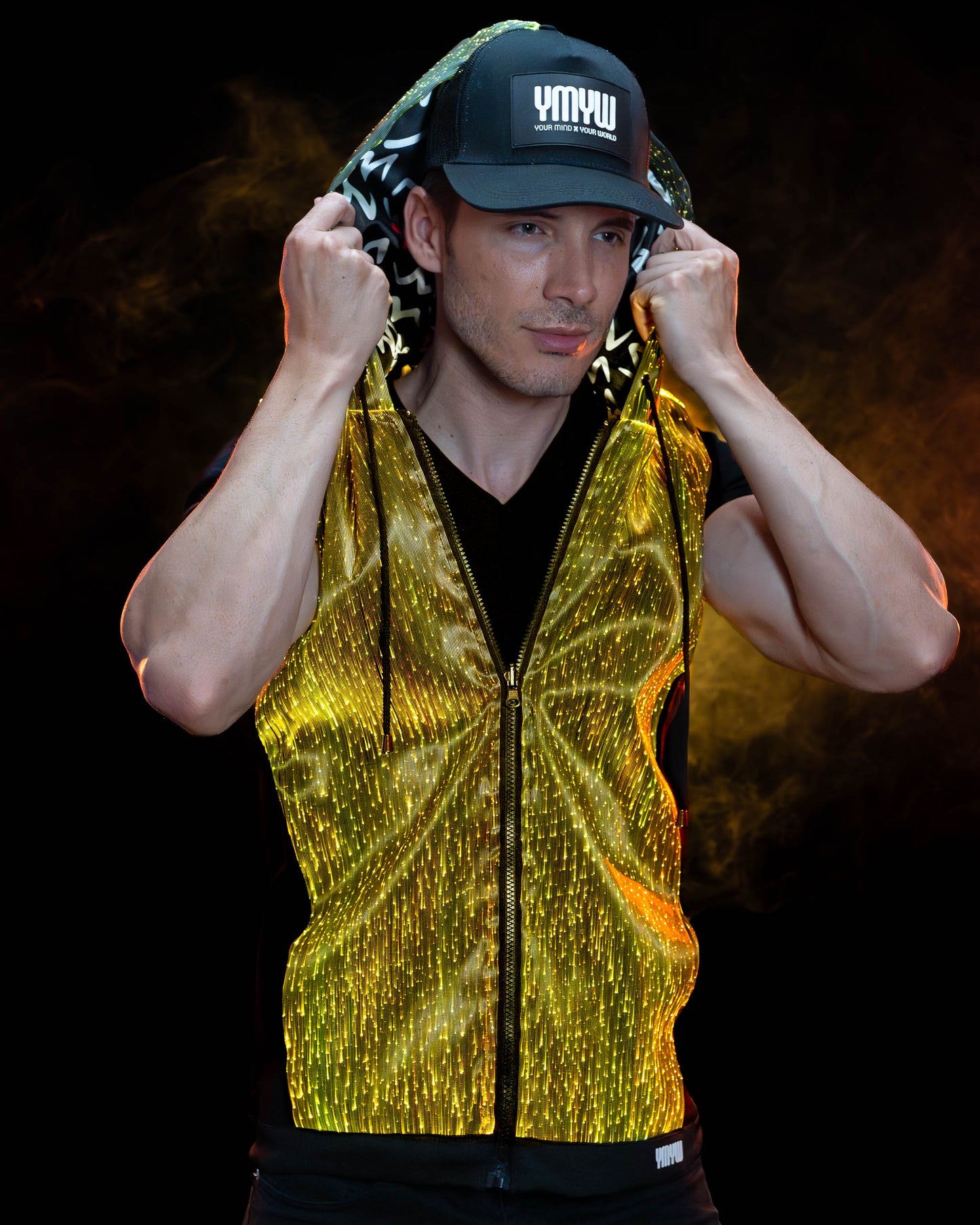 Man wearing a fiber optic light-up sleeveless hoodie illuminated in gold light against a dark background