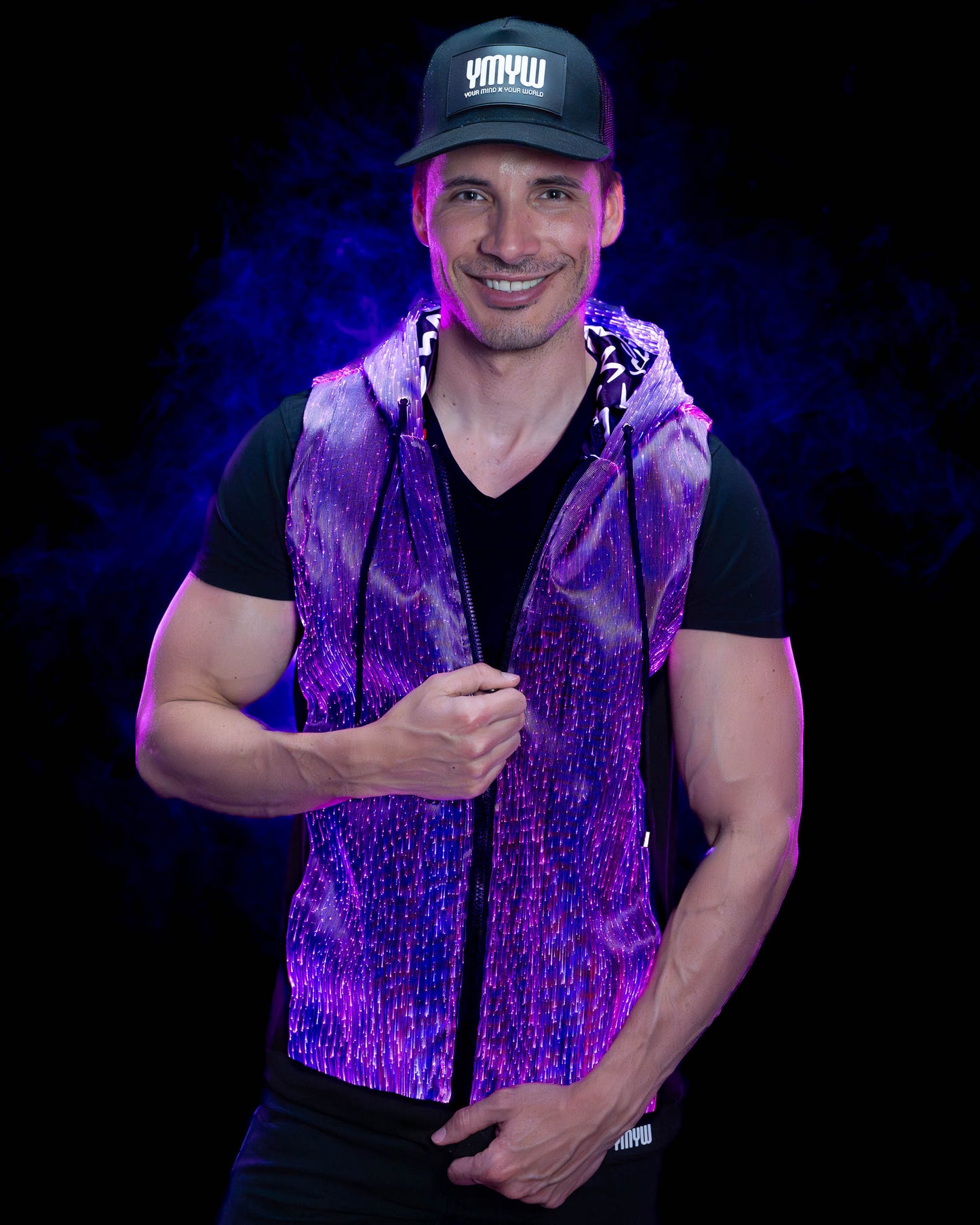 Man wearing a fiber optic light-up sleeveless hoodie illuminated in purple light against a dark background