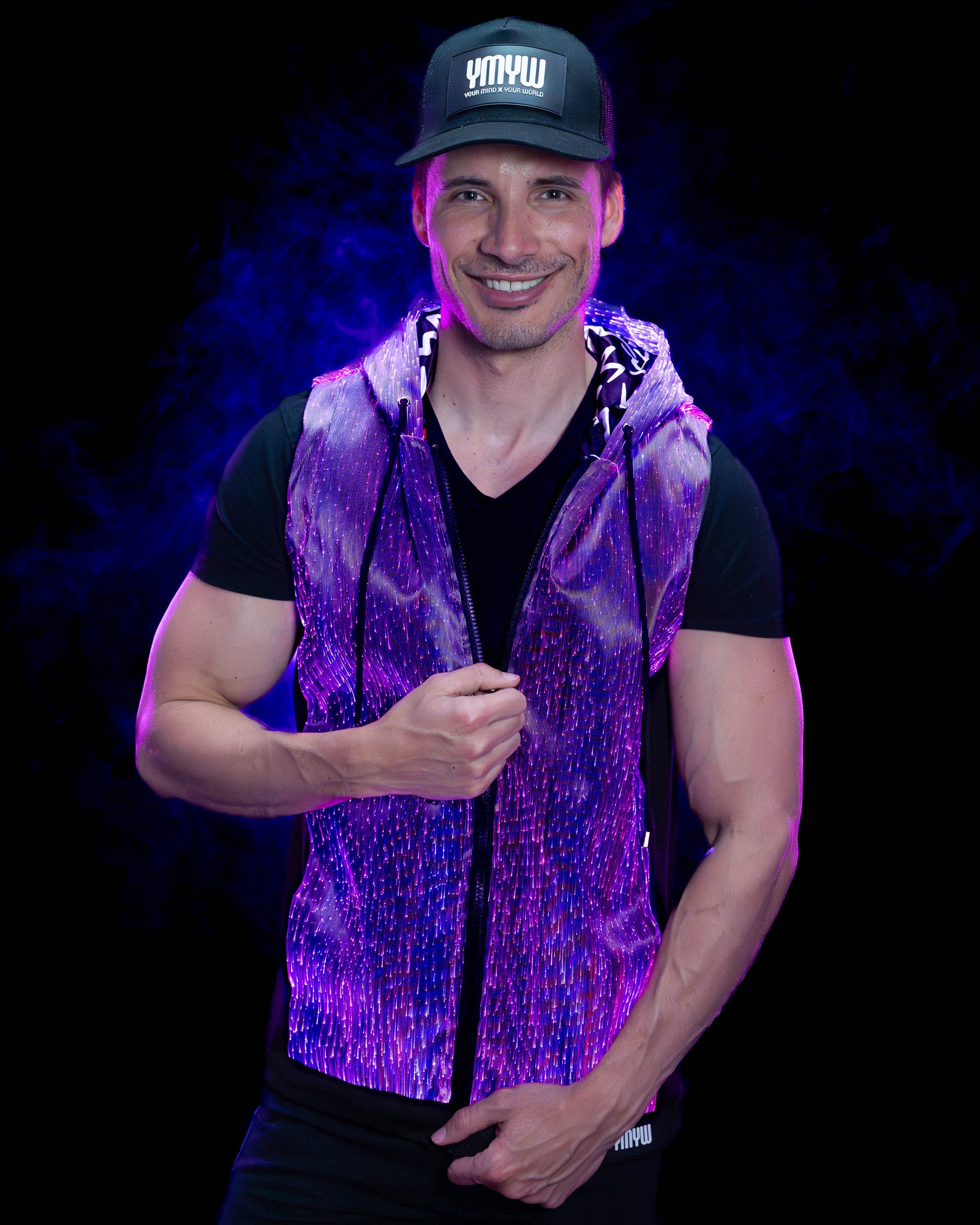 Man wearing a fiber optic light-up sleeveless hoodie illuminated in purple light against a dark background