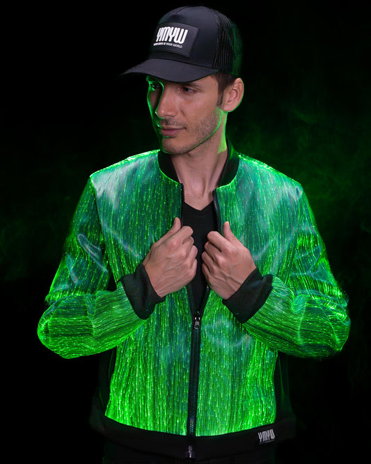 Man wearing a fiber optic bomber jacket illuminated in green light with a black cap, against a dark background