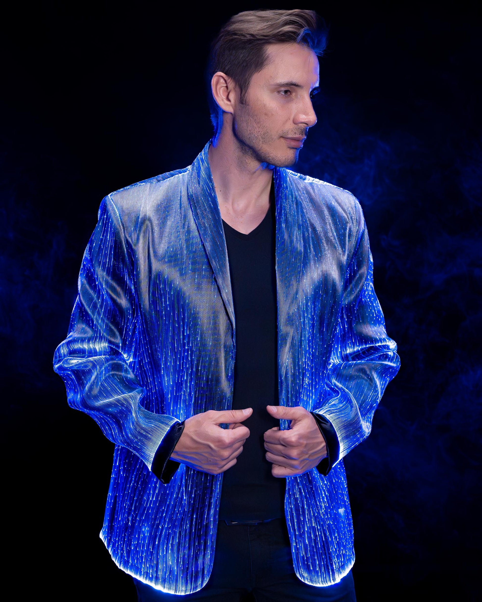 Man wearing a fiber optic light-up suit jacket illuminated in blue light against a dark background