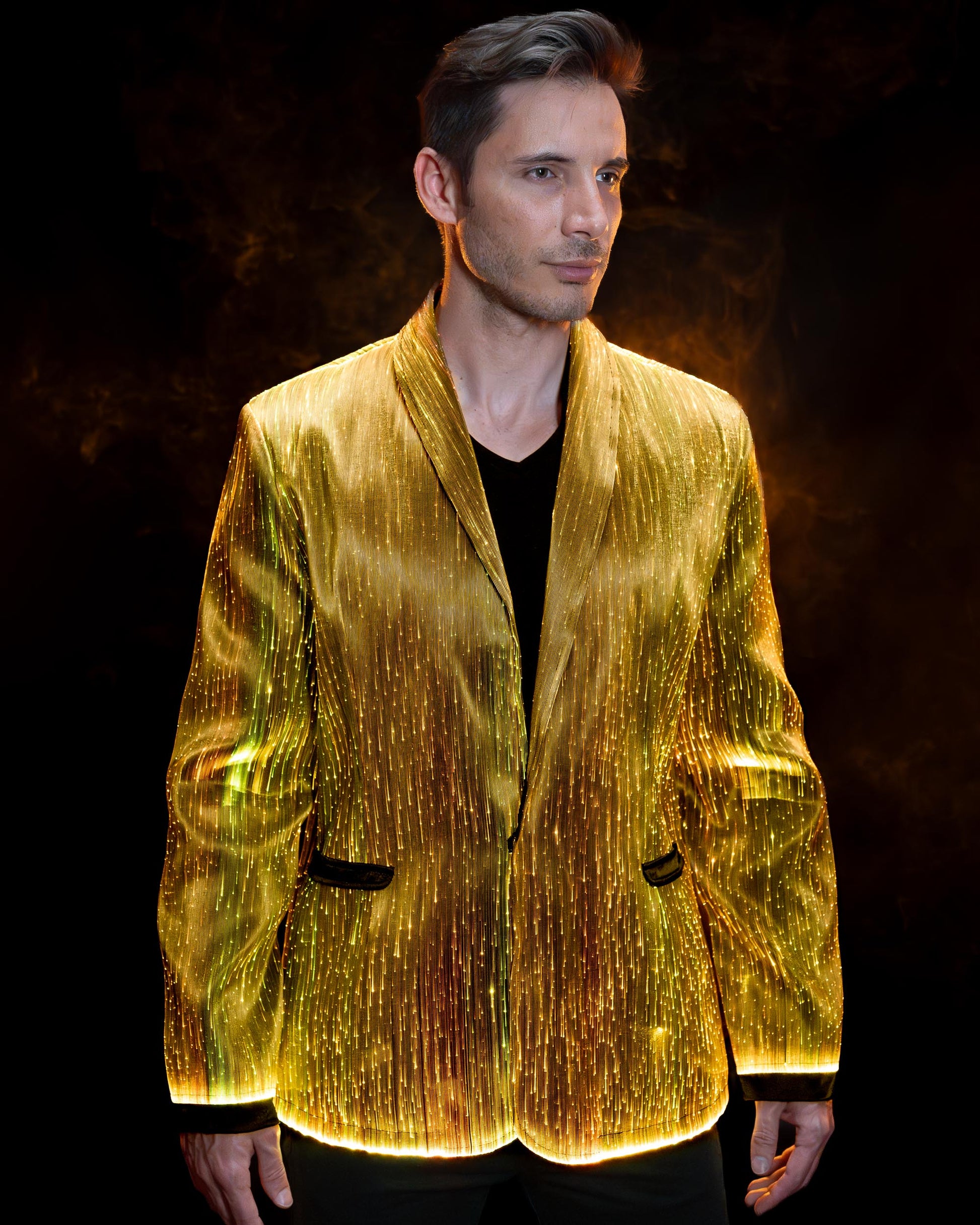 Man wearing a fiber optic light-up suit jacket illuminated in gold light against a dark background