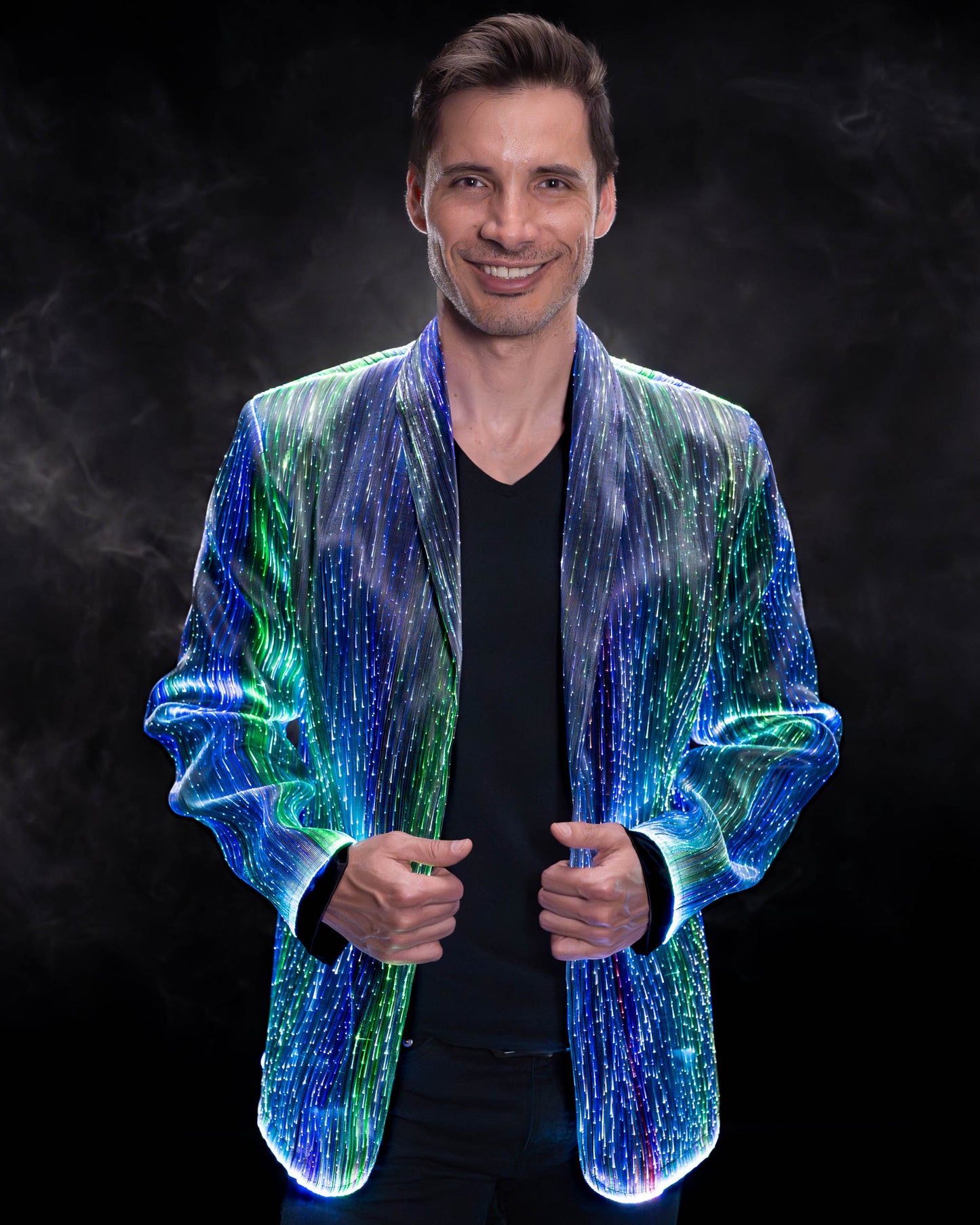Man wearing a fiber optic light-up suit jacket illuminated in blue and green light against a dark background
