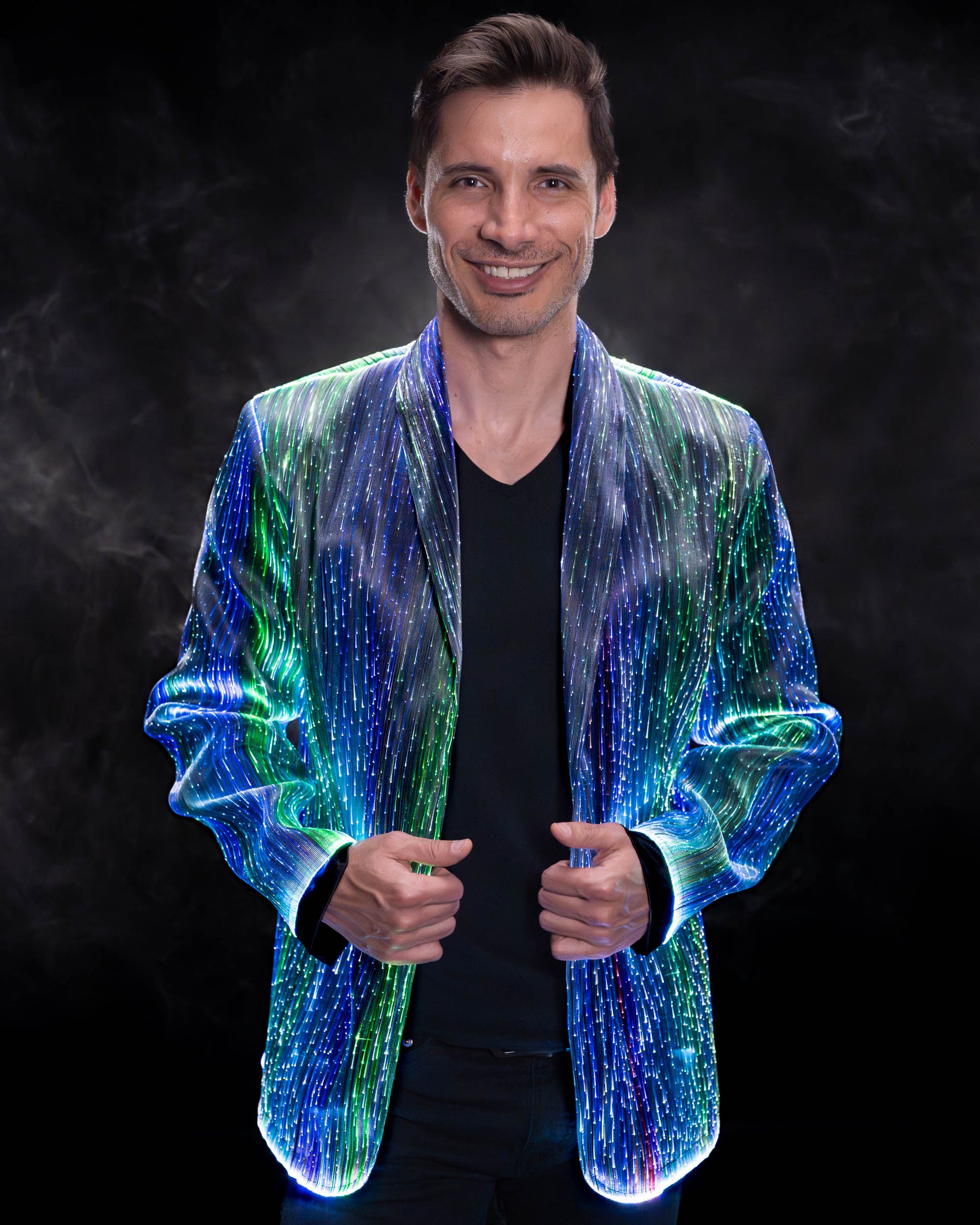Man wearing a fiber optic light-up suit jacket illuminated in blue and green light against a dark background