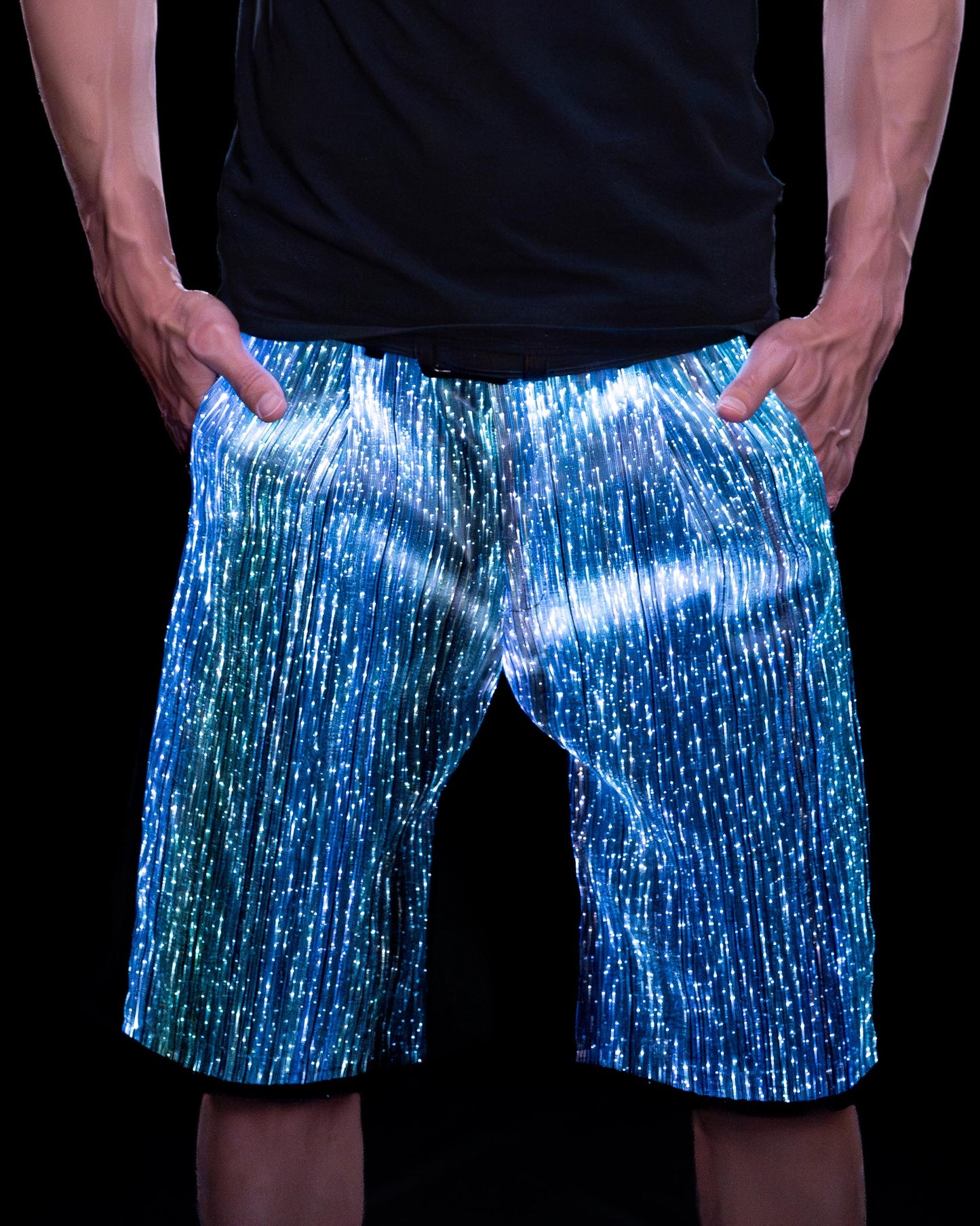 Man wearing black fiber optic light up shorts glowing in light blue against a dark background
