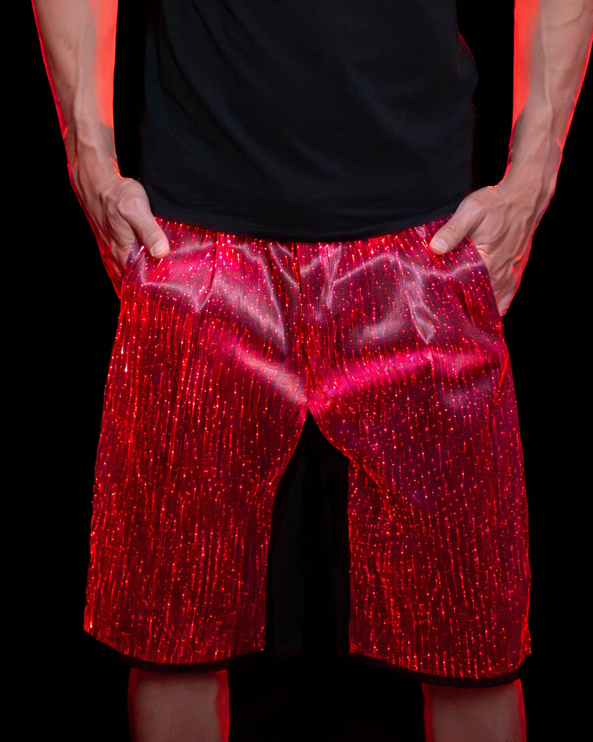 Man wearing black fiber optic light up shorts glowing in red light against a dark background