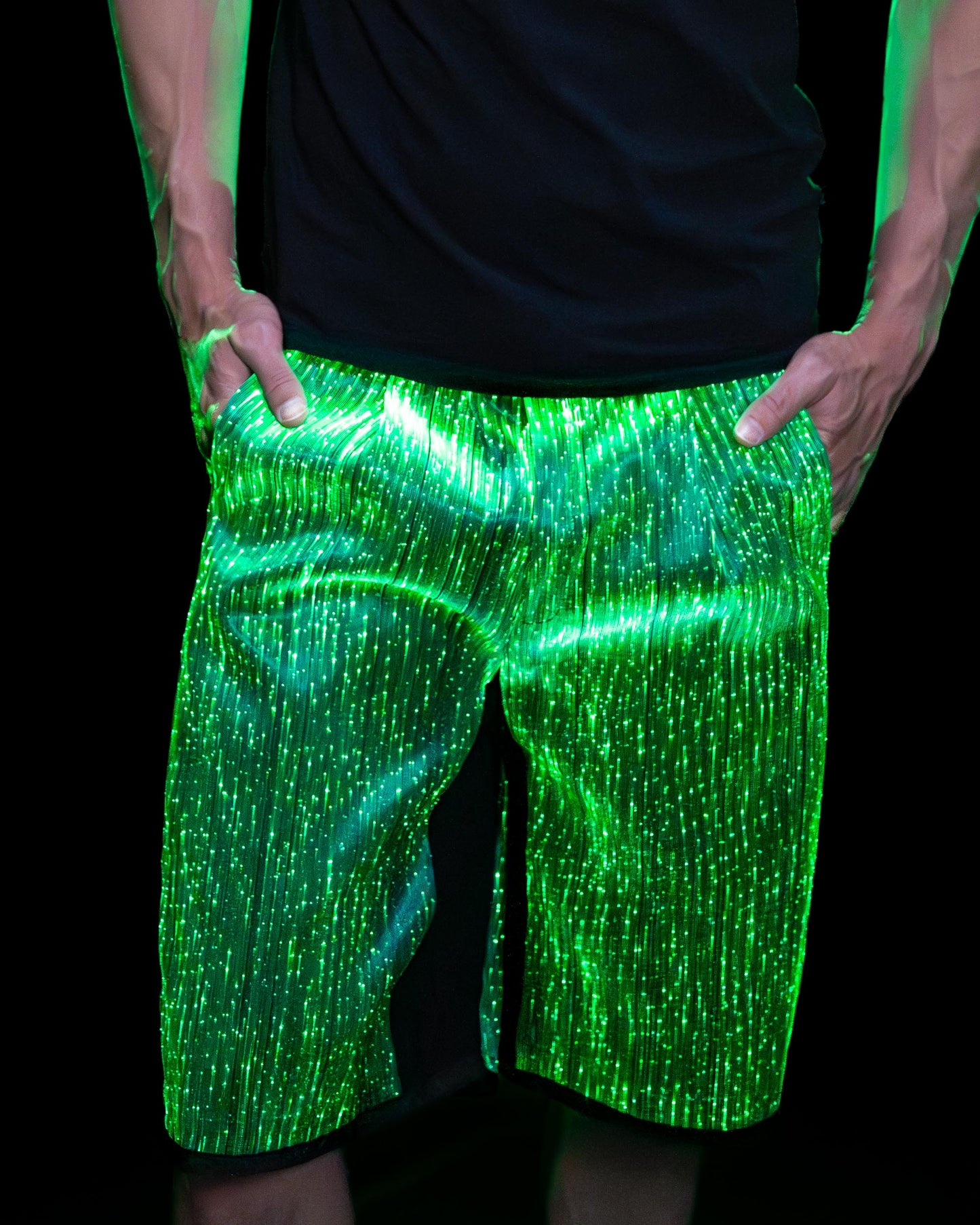 Man wearing black fiber optic light up shorts glowing in green light against a dark background