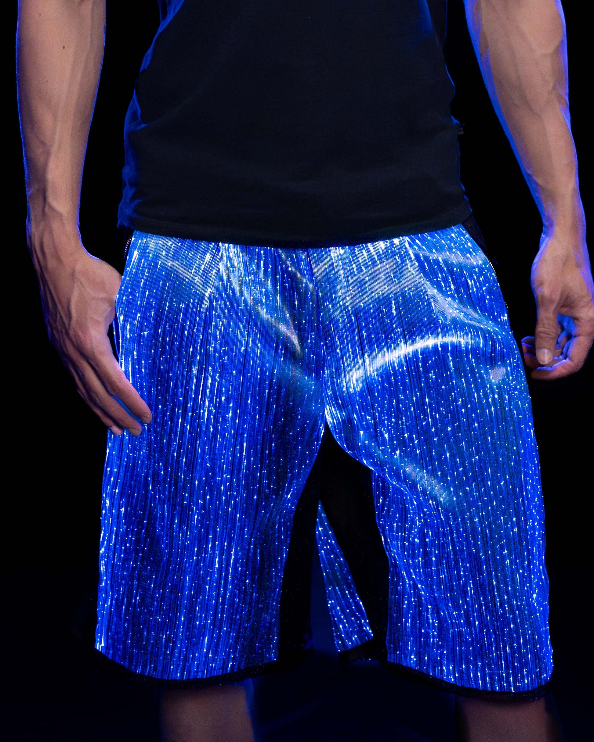 Man wearing black fiber optic light up shorts glowing in blue light against a dark background