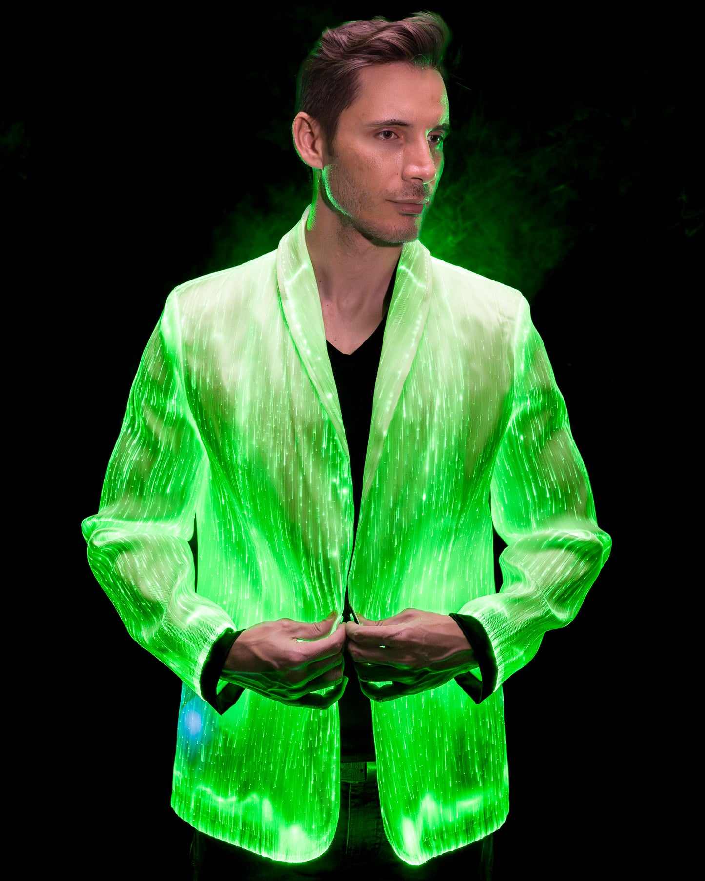 Man wearing a white fiber optic light up suit jacket glowing in green light against a dark background