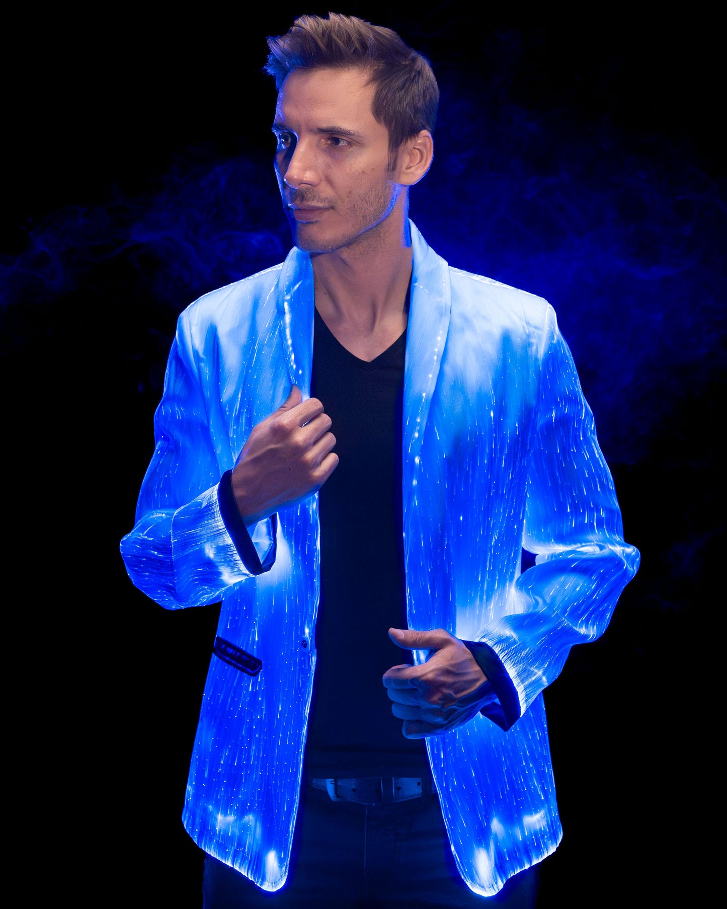 Man wearing a white fiber optic light up suit jacket glowing in blue light against a dark background