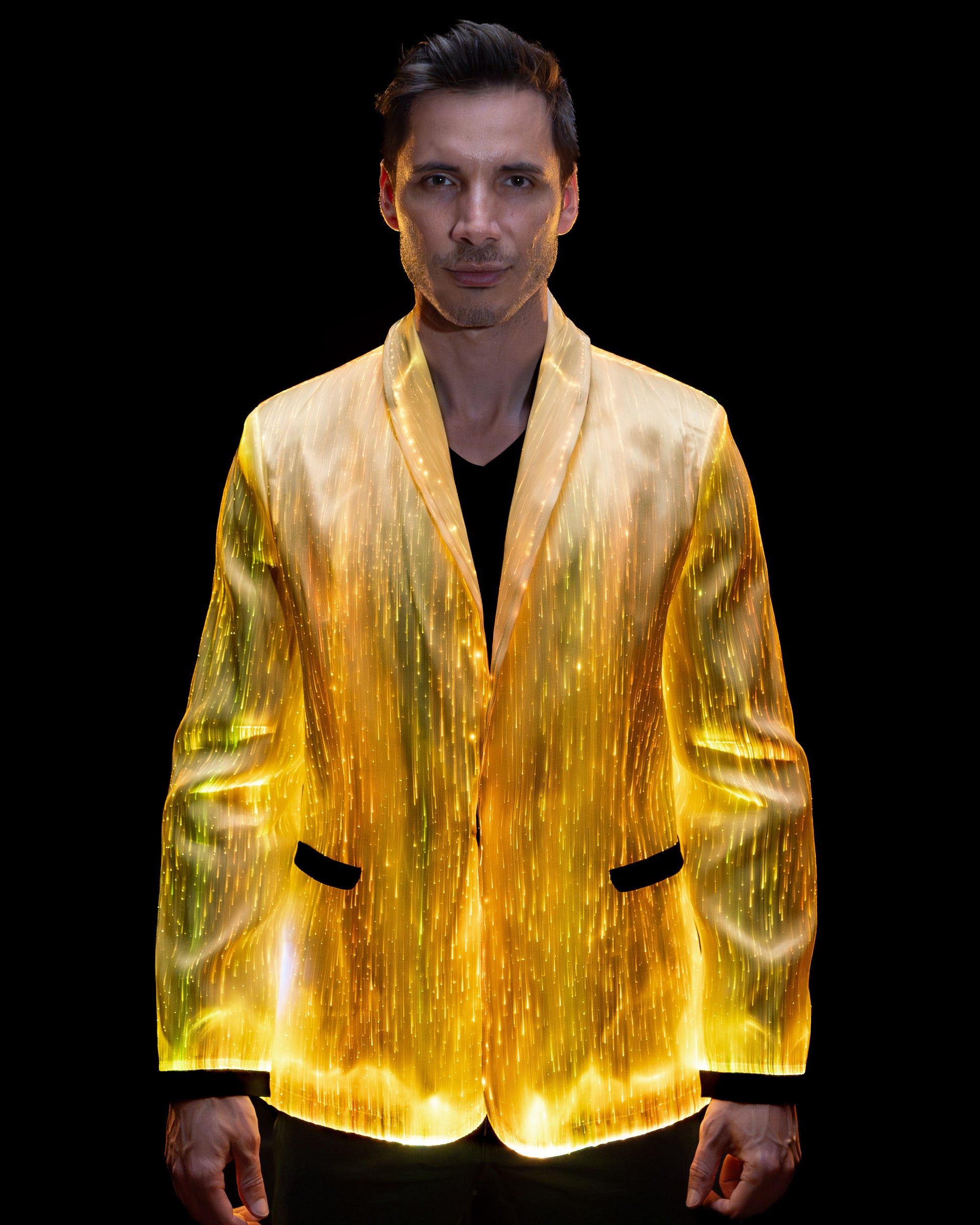 Man wearing a white fiber optic light up suit jacket glowing in golden light against a dark background