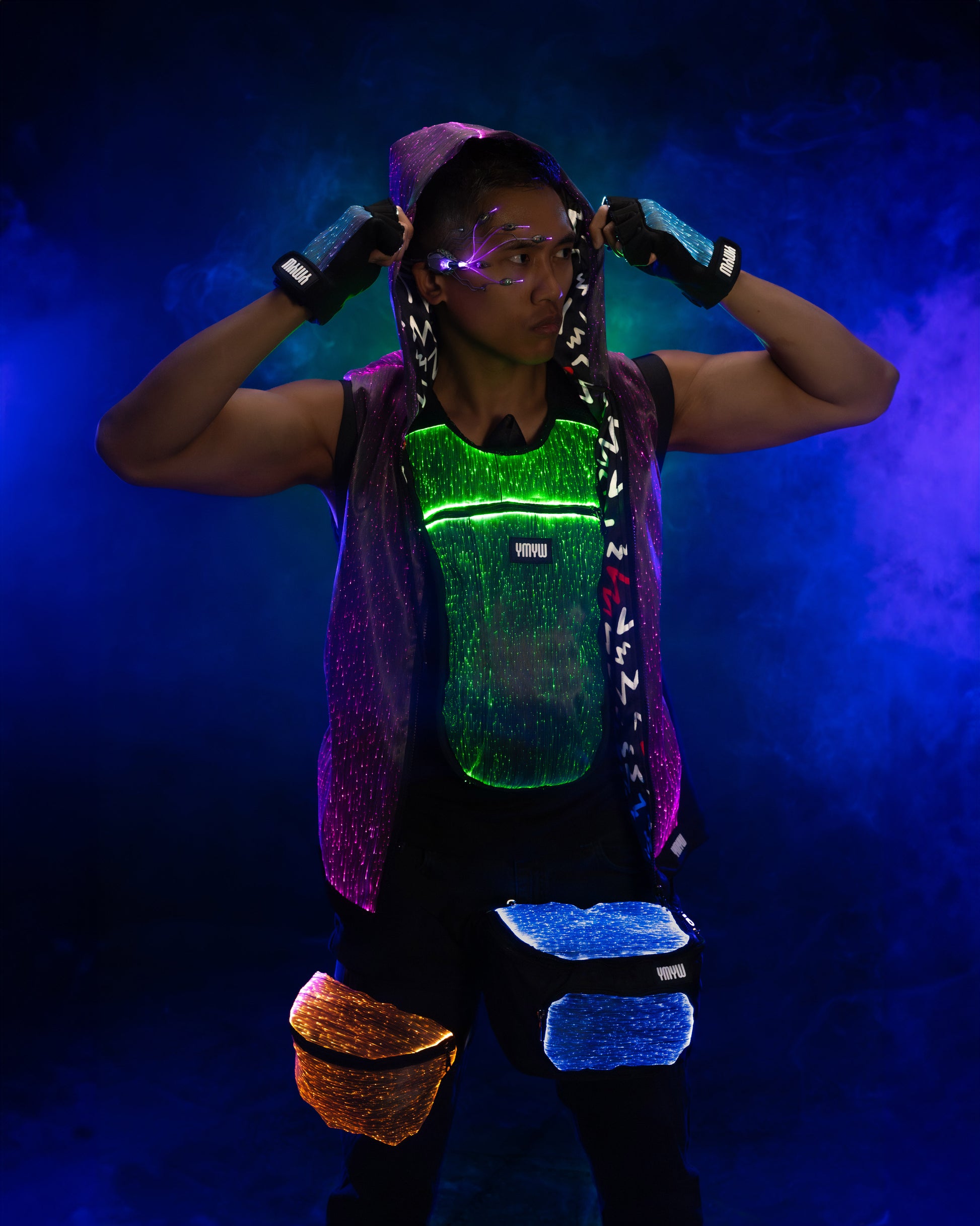 Man wearing fiber optic light up vest and fanny pack illuminated in green, blue, and orange light against a dark background