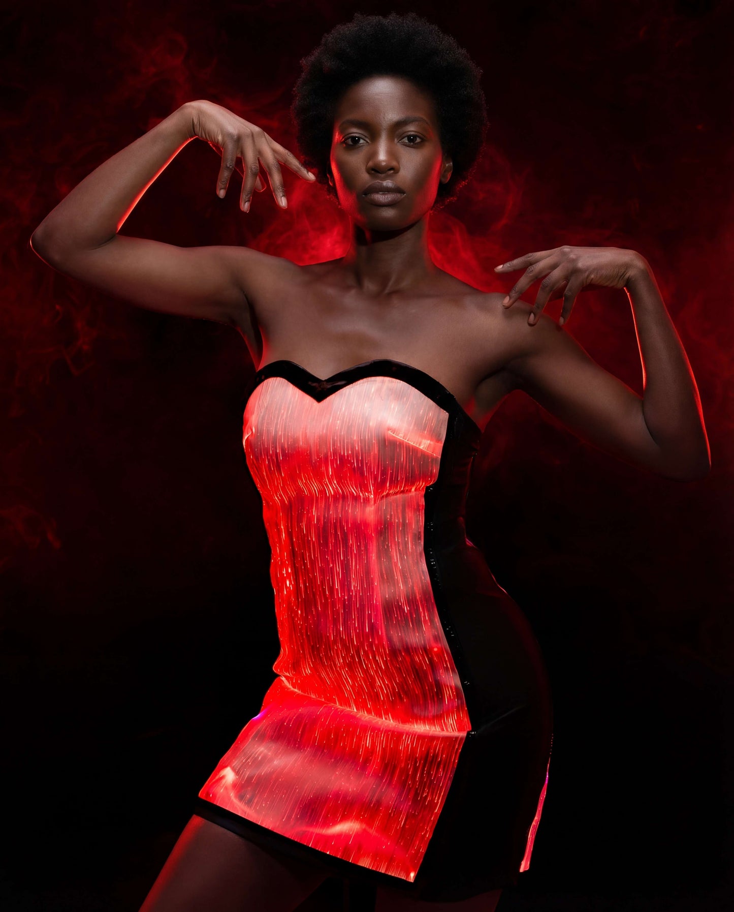 Model wearing a strapless red fiber-optic illuminated dress, posing with raised arms against a dark smoky background