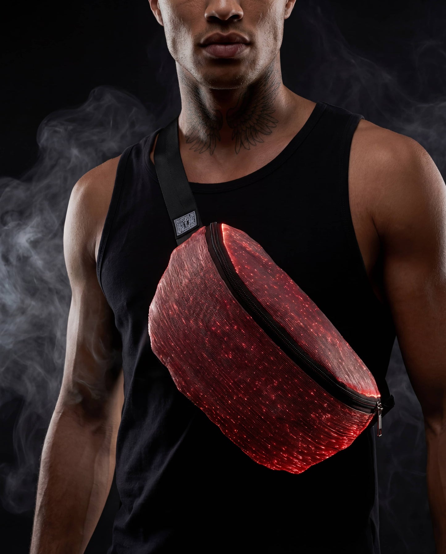 Man wearing a black tank top with a glowing red fiber-optic fanny pack worn crossbody against a dark, smoky background