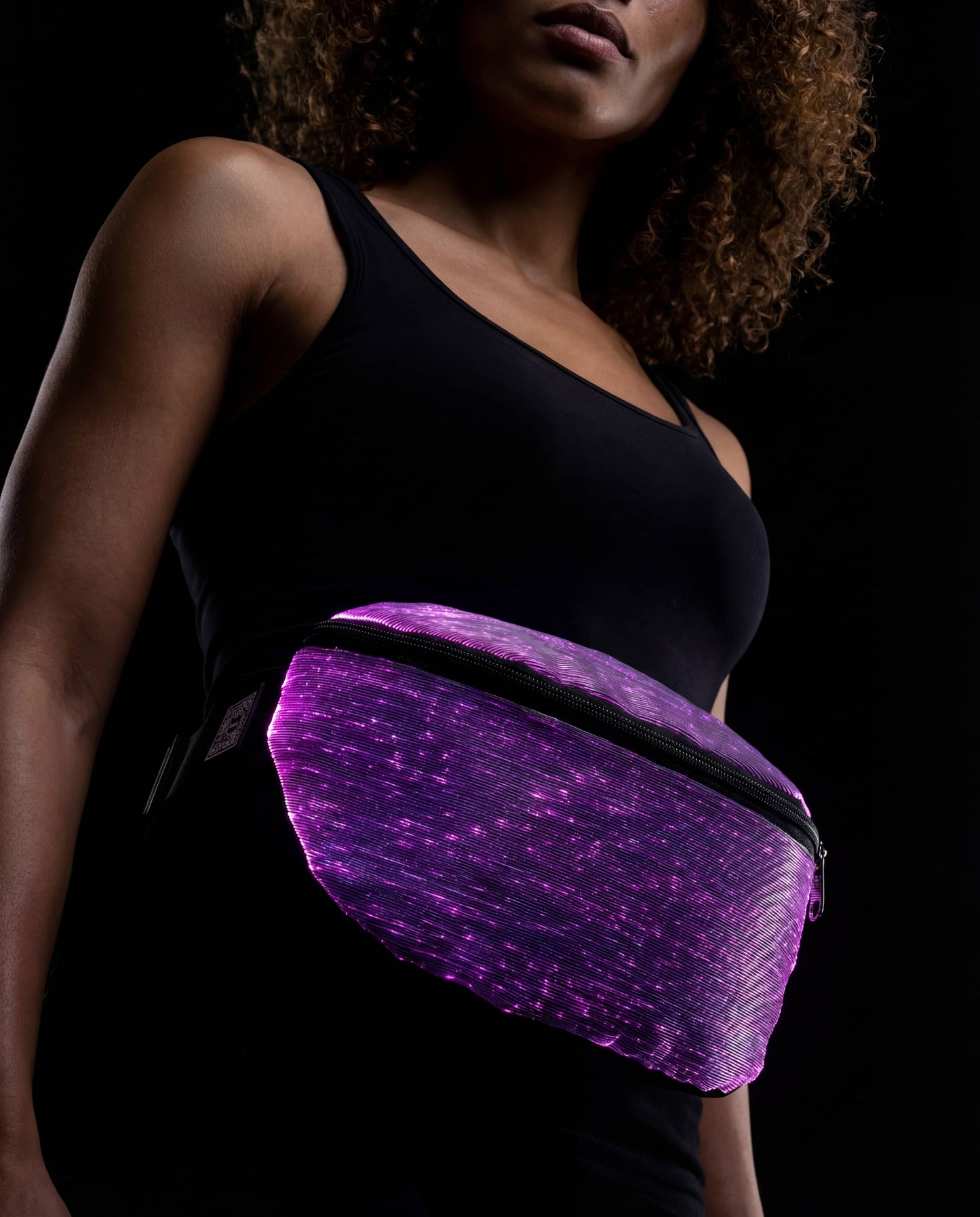 Purple fiber-optic fanny pack glowing against a dark background, worn across the waist over a black top