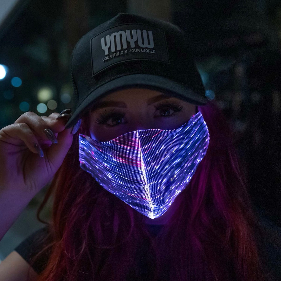 Woman wearing a YMYW cap and a fiber optic light-up mask illuminated in purple light against a dark background