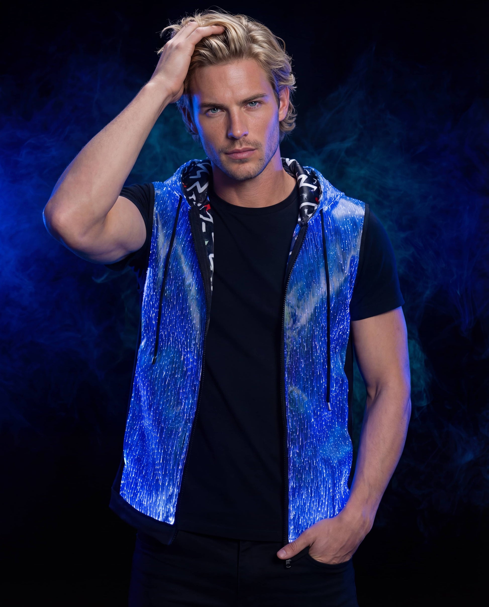 Man wearing a glowing blue sleeveless fiber-optic hoodie, standing against a dark blue smoke-filled background with one hand in his hair