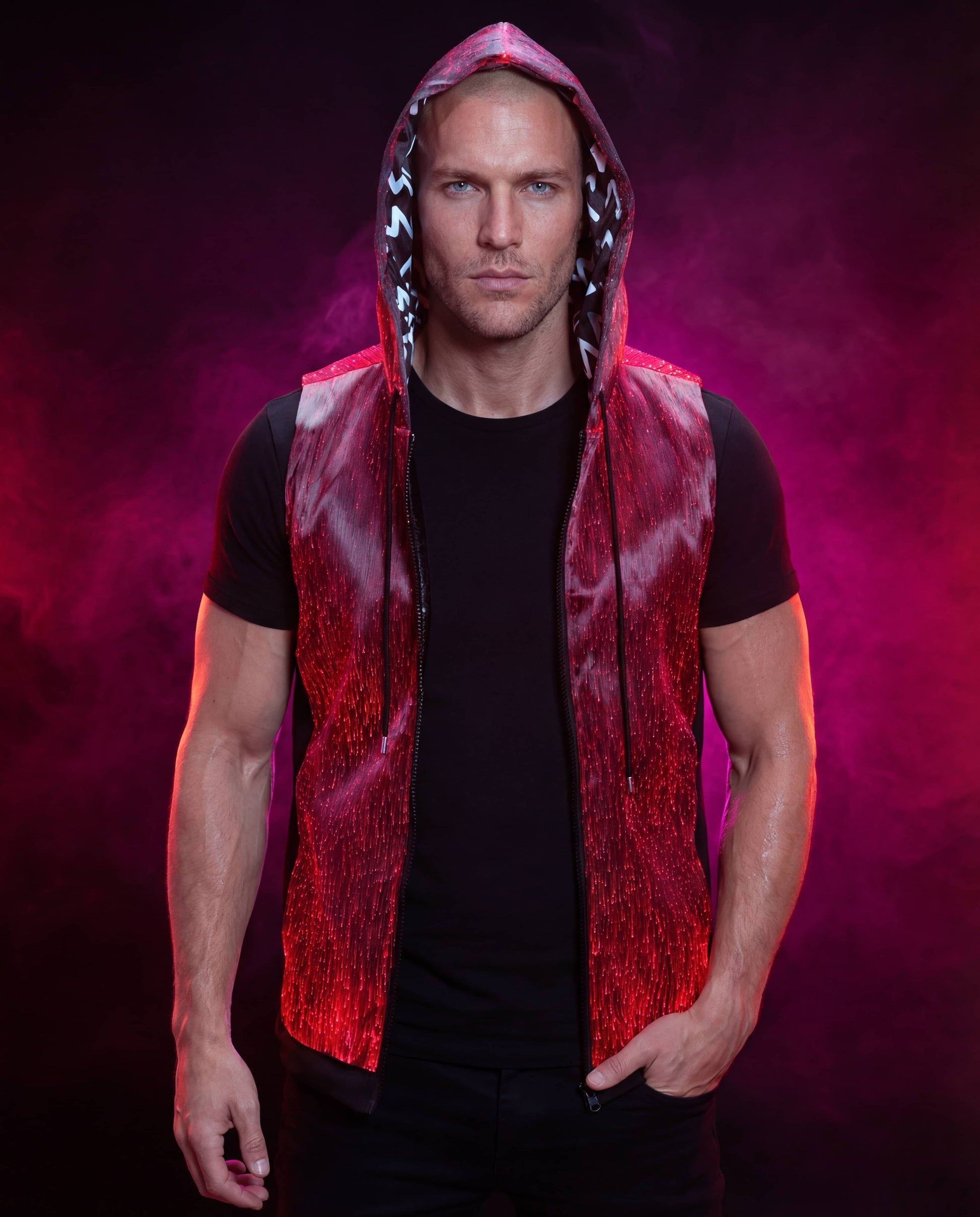Man wearing a glowing red sleeveless fiber-optic hoodie, standing against a dark pink smoke-filled background