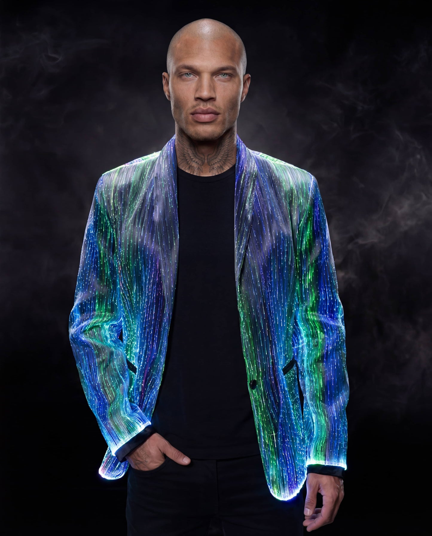 Man wearing a glowing blue and green fiber-optic suit jacket, standing against a dark smoky background
