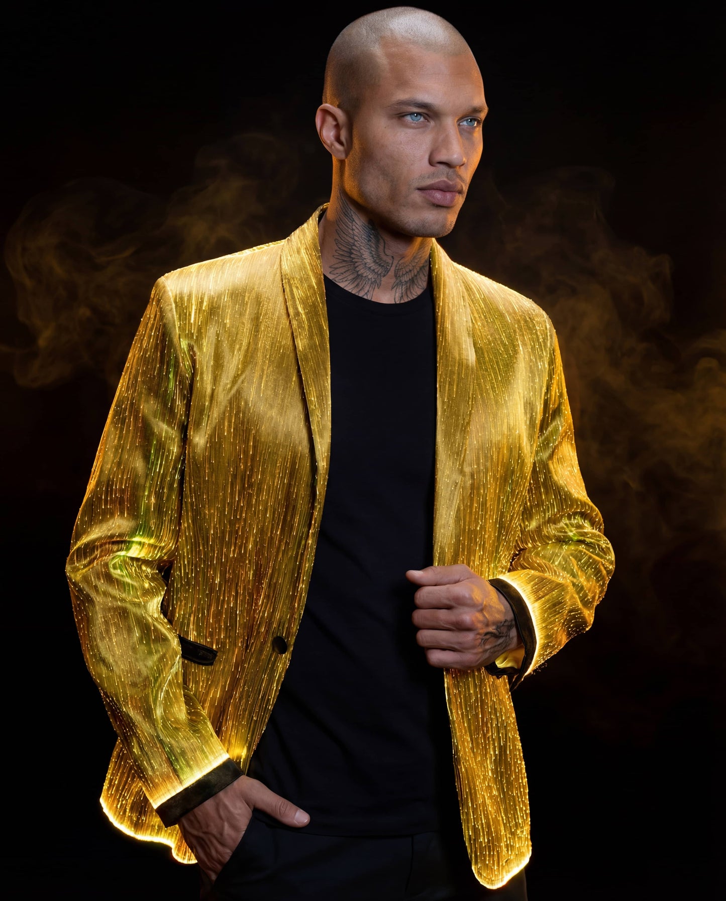 Man wearing a glowing gold fiber-optic suit jacket, standing against a dark background with warm smoke behind him