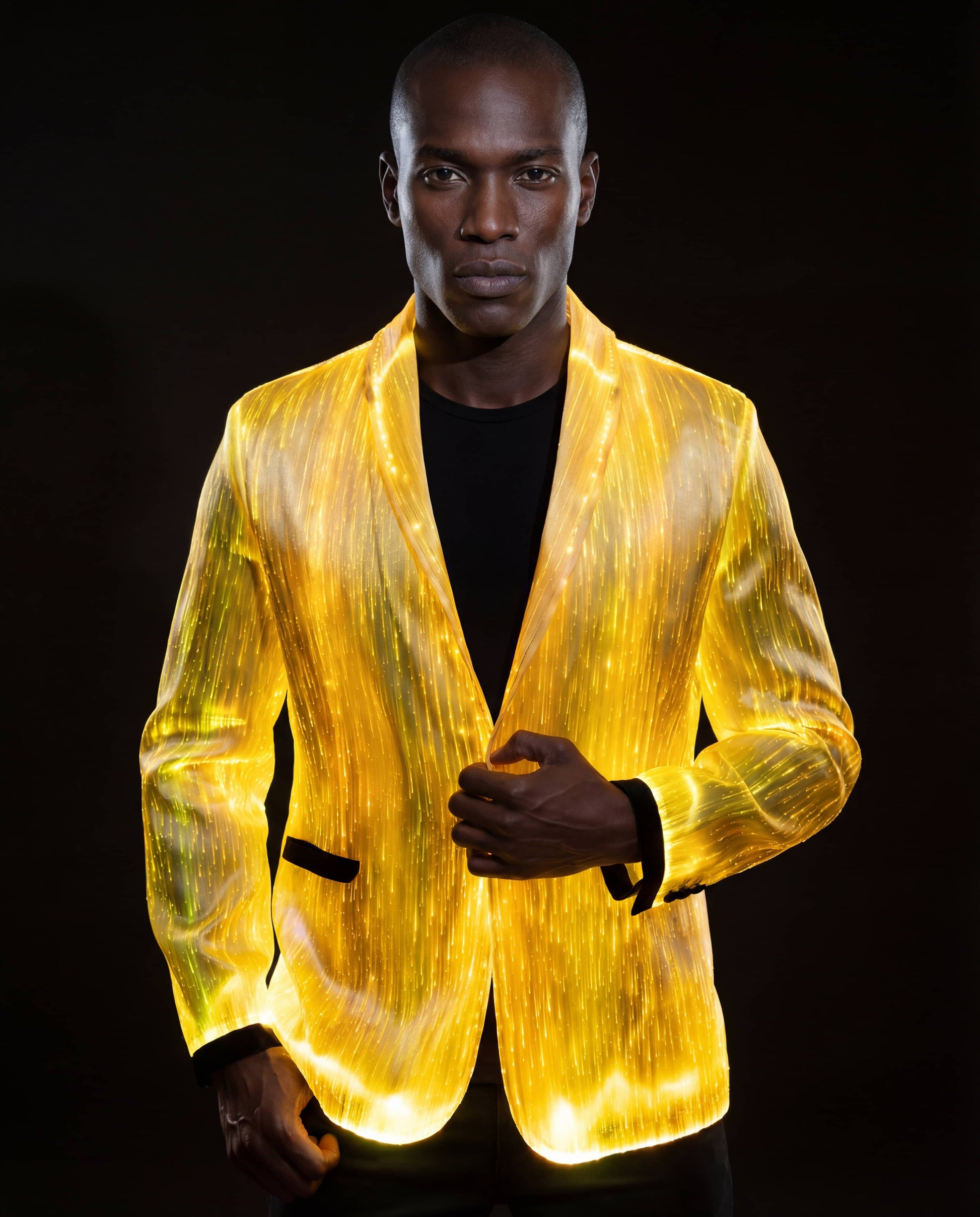 Man wearing a glowing gold fiber-optic suit jacket, standing against a dark background with warm light illuminating the fabric