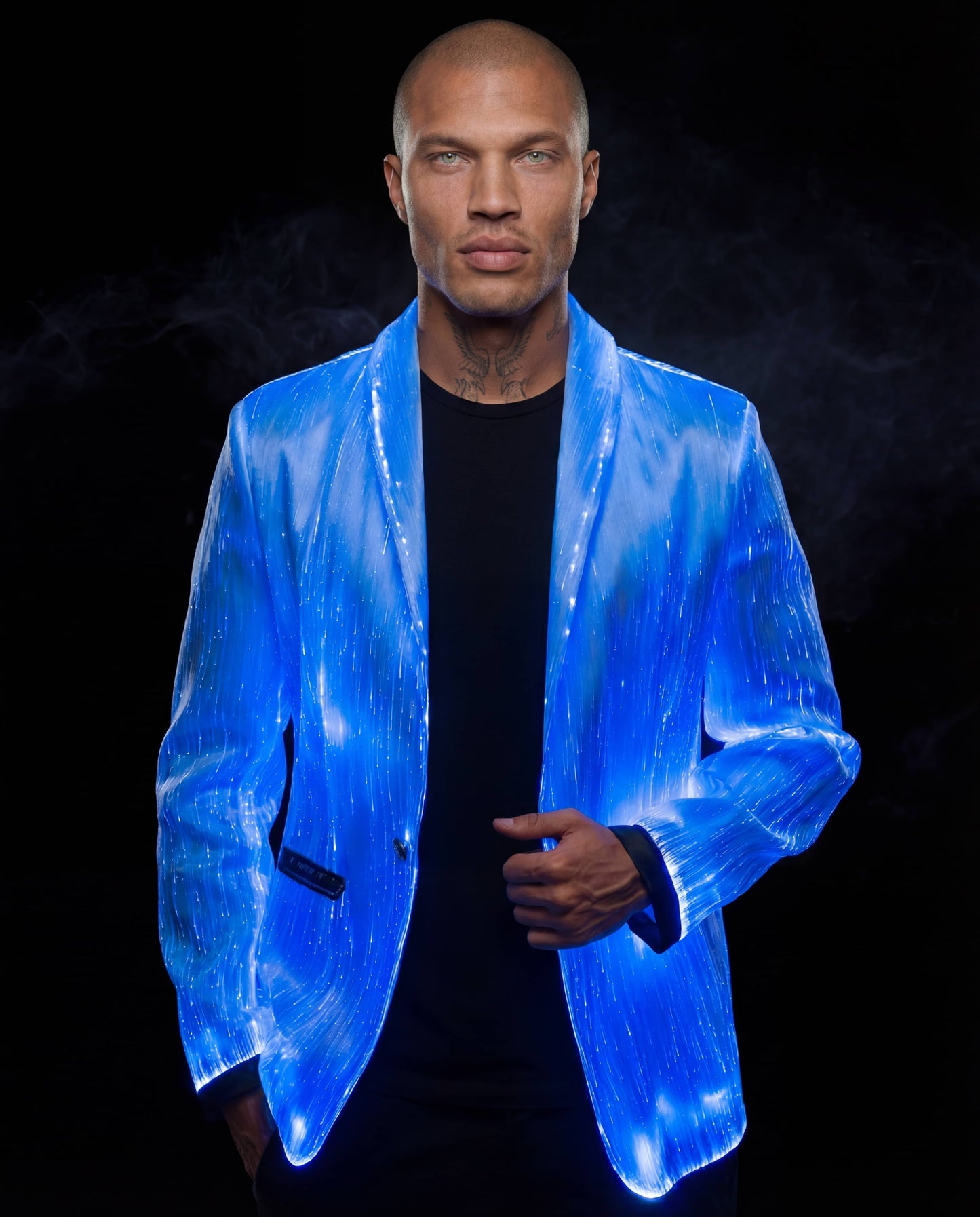 Man wearing a glowing blue fiber-optic suit jacket, standing against a dark smoky background with one hand touching the front of the jacket