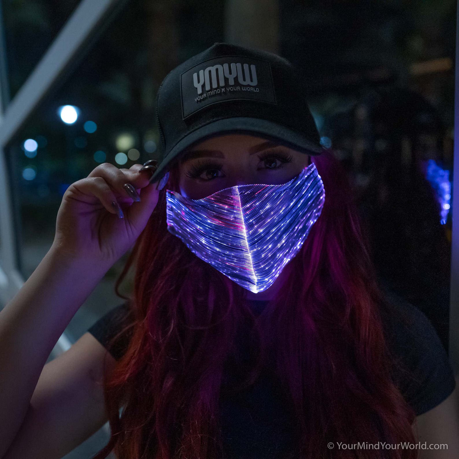 Woman wearing a YMYW cap and a fiber optic light-up mask illuminated in purple light against a dark background
