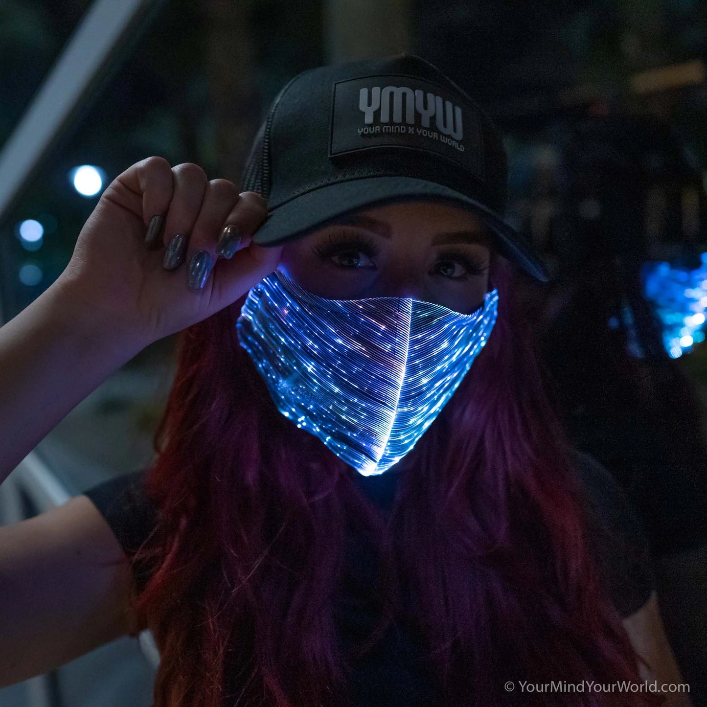 Woman wearing a YMYW cap and a fiber optic light-up mask illuminated in light blue light against a dark background