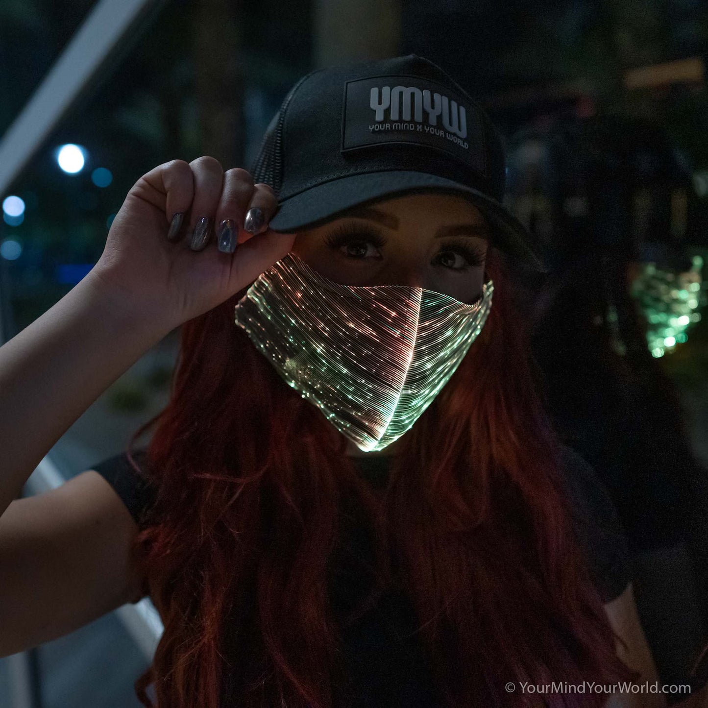Woman wearing a YMYW cap and a fiber optic light-up mask illuminated in gold light against a dark background