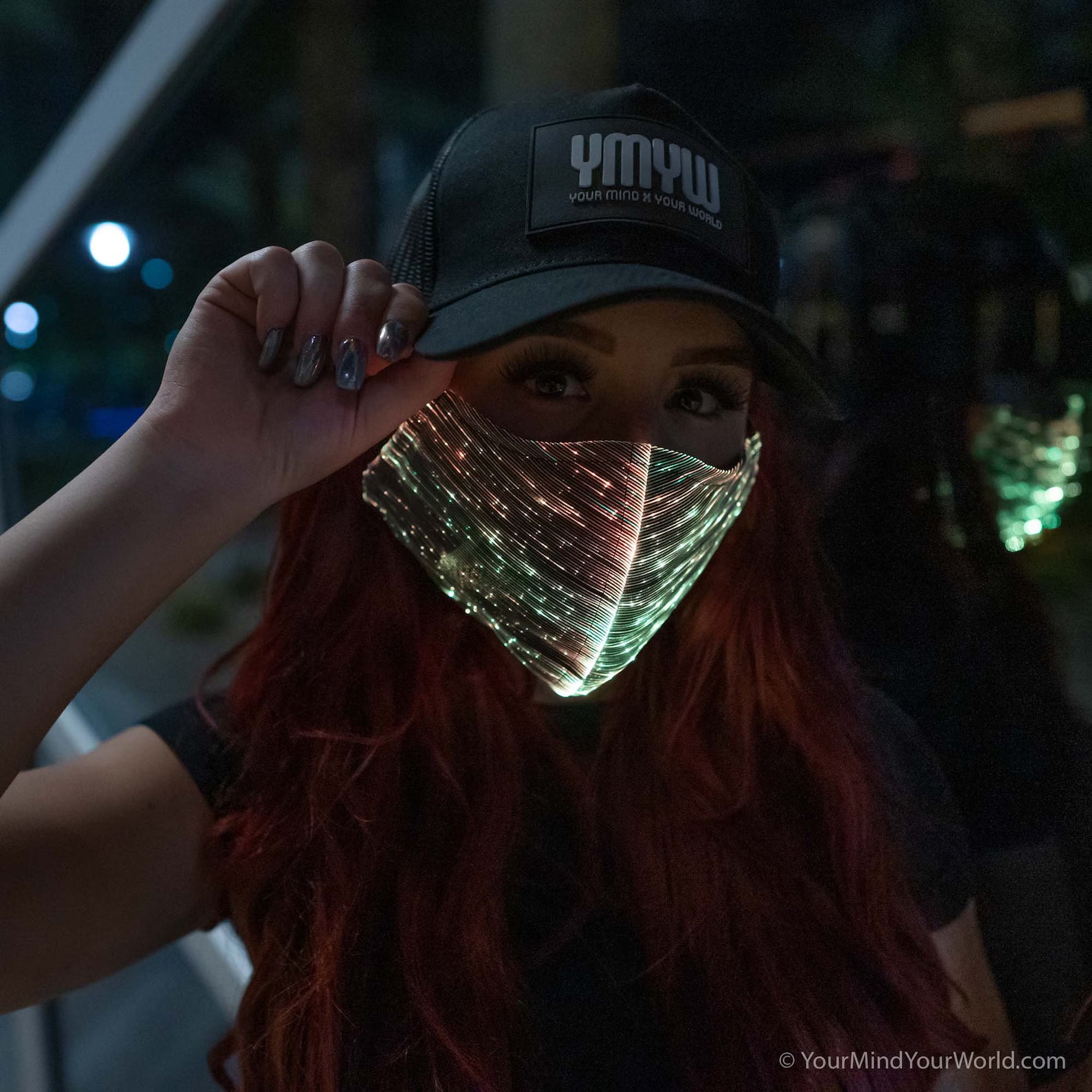 Woman wearing a YMYW cap and a fiber optic light-up mask illuminated in gold light against a dark background