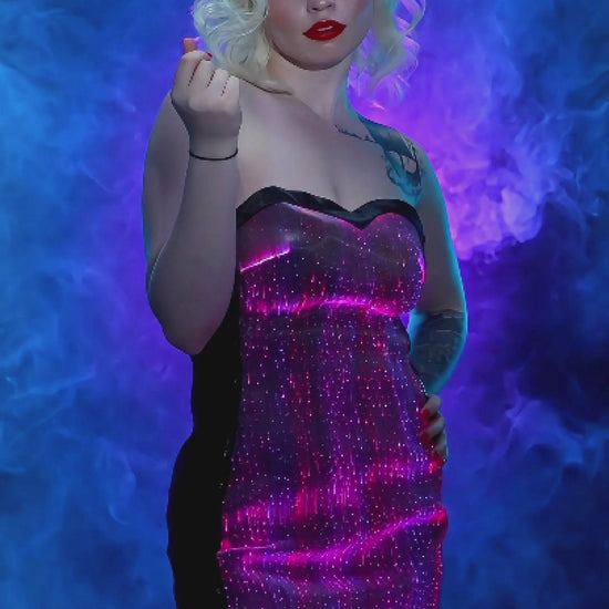 Woman wearing a strapless fiber-optic LED dress that glows in muliple colors while standing against a blue smoky background