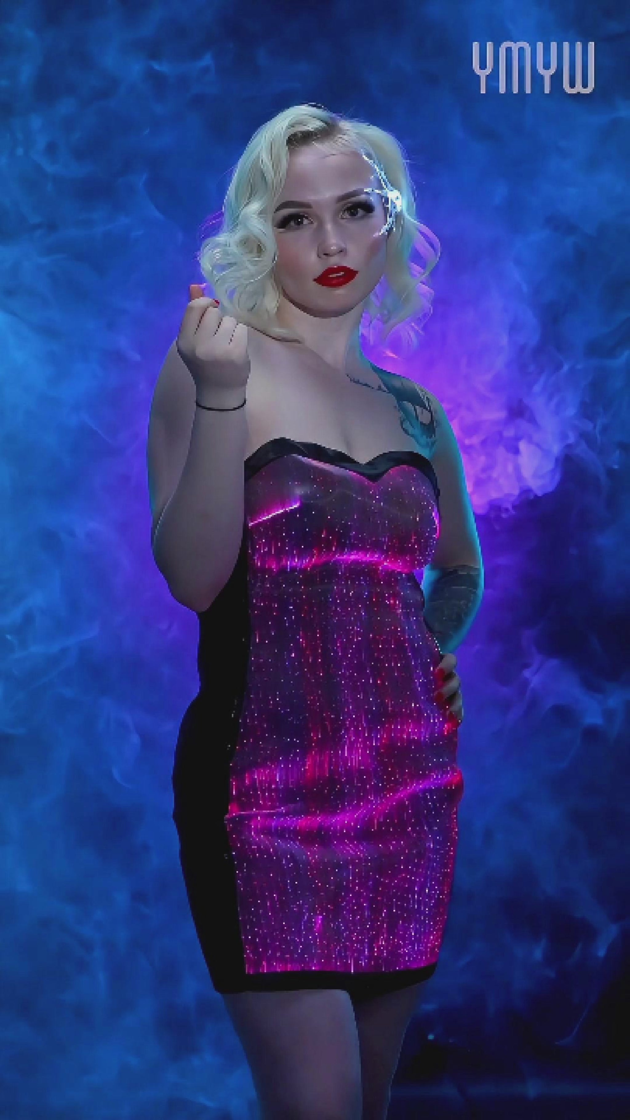 Woman wearing a strapless fiber-optic LED dress that glows in muliple colors while standing against a blue smoky background
