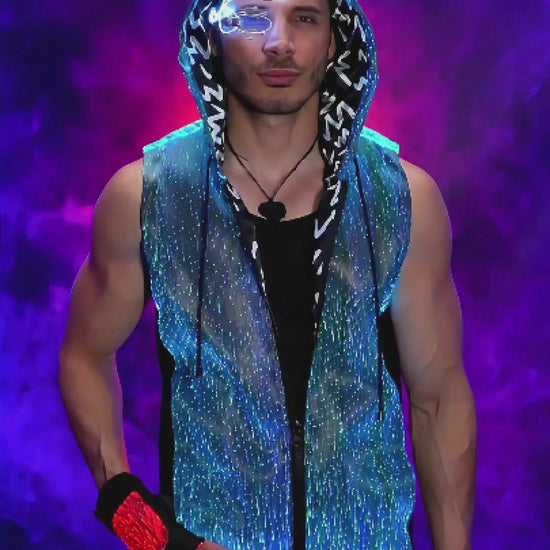 Man wearing a fiber optic LED sleeveless hoodie that glows in shifting colors while he spins slowly on a turntable platform against a backlit smoky background