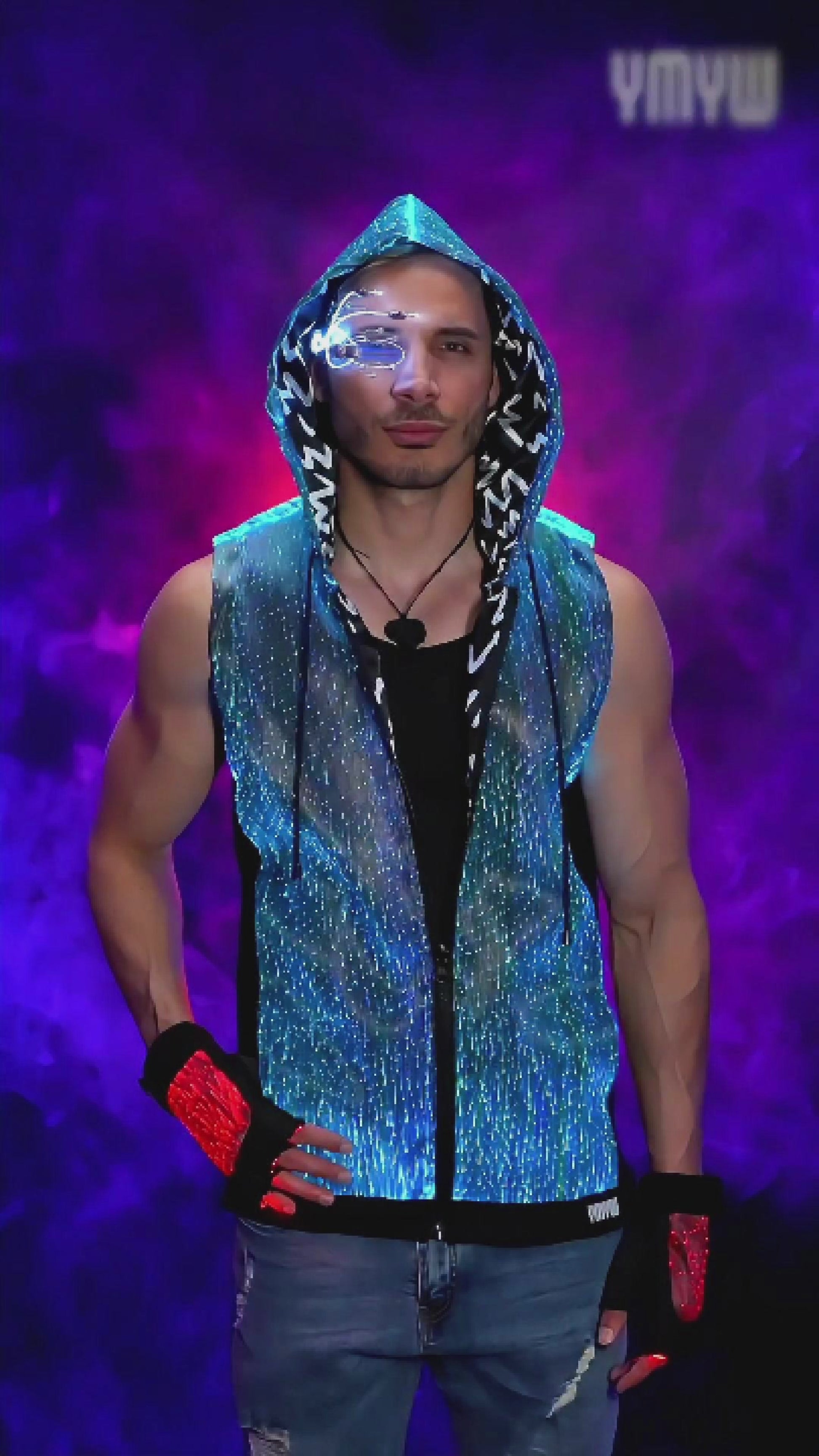 Man wearing a fiber optic LED sleeveless hoodie that glows in shifting colors while he spins slowly on a turntable platform against a backlit smoky background