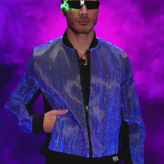 Man wearing a fiber optic LED bomber jacket rotating on a platform, the jacket glowing in shifting colors against a dark studio background