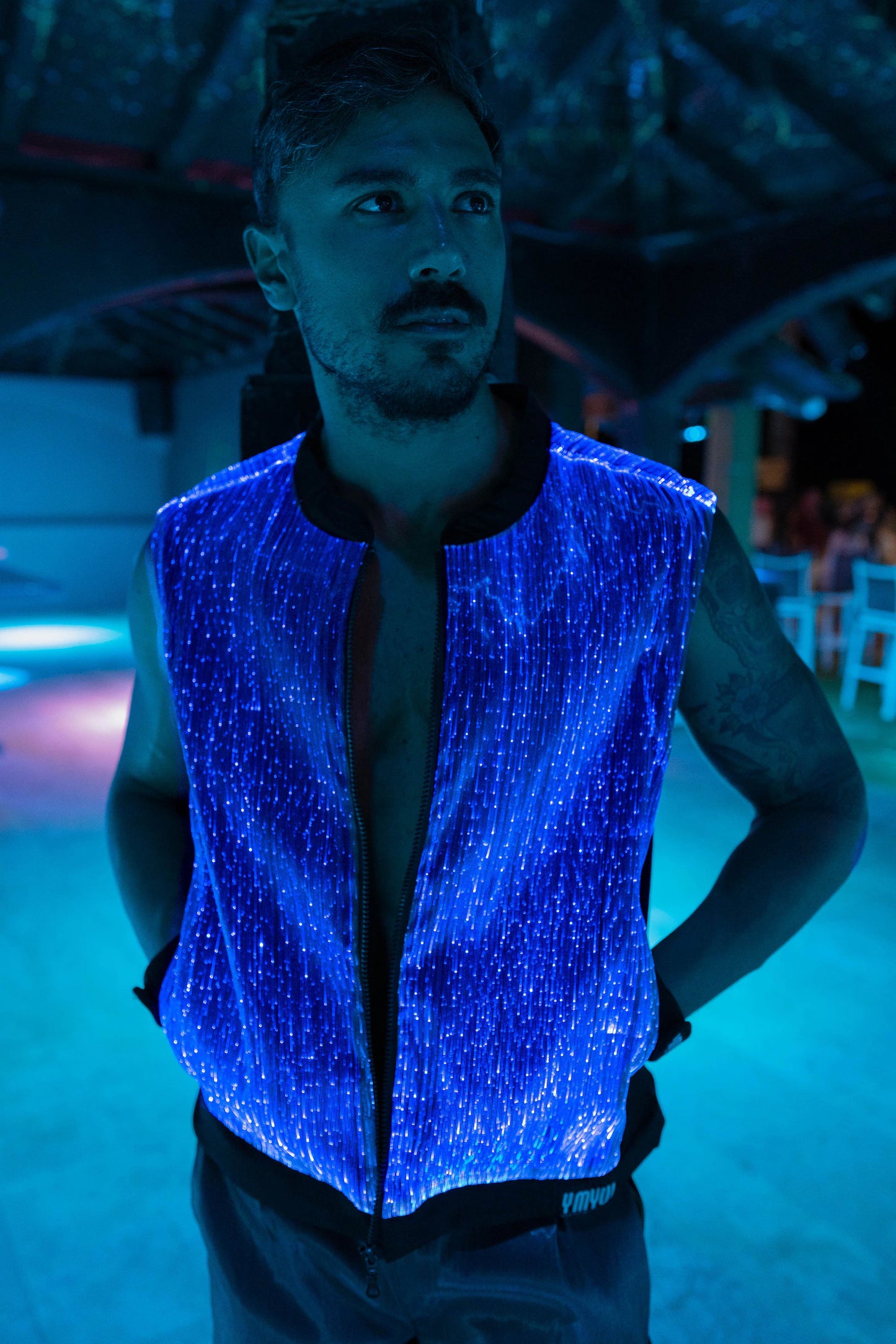 Man wearing a black fiber optic light up vest illuminated in blue light against a dark background